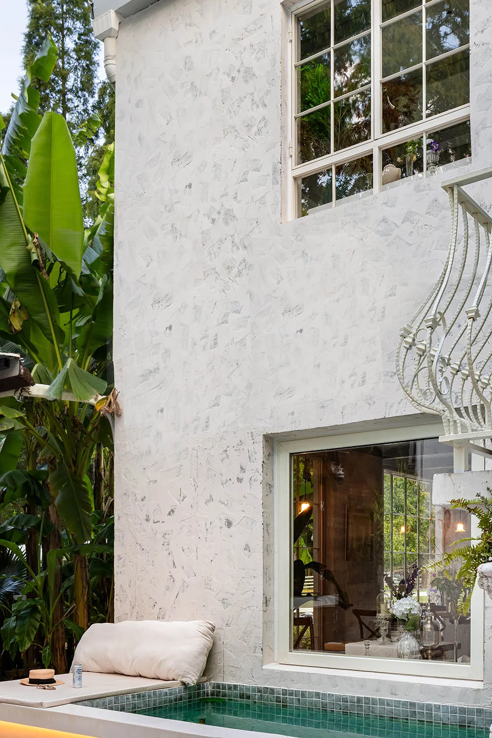 White stucco exterior of a minimalist residential outdoor space with a pool and greenery.