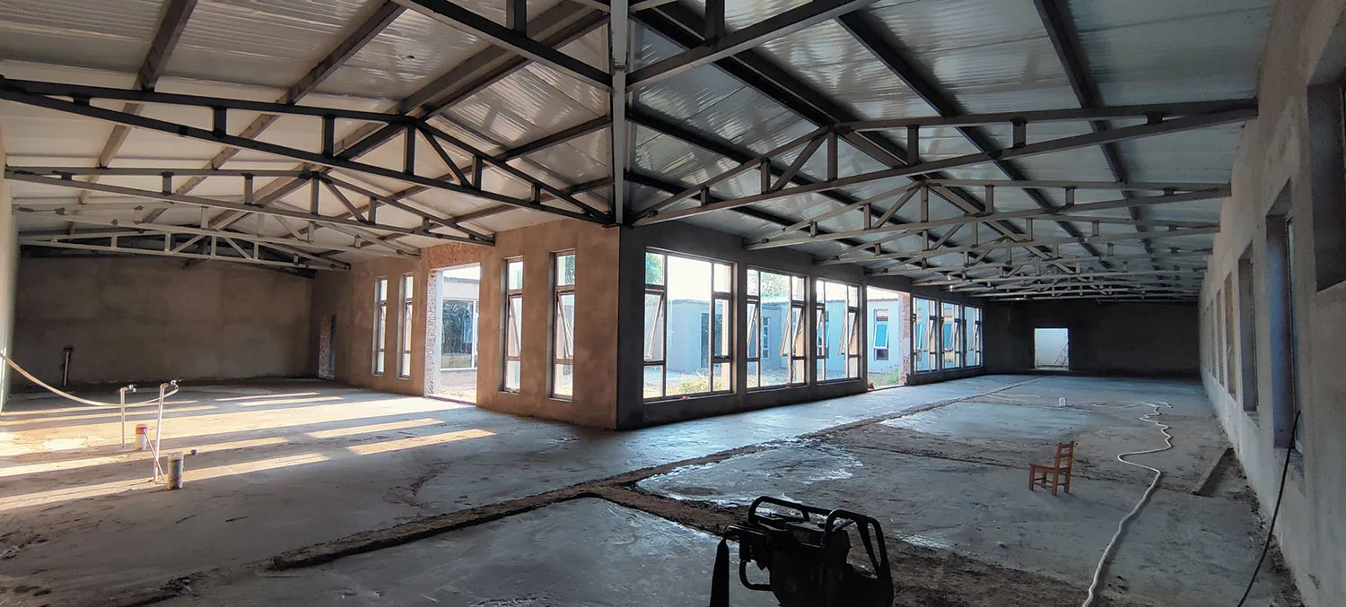 A large, industrial-style building with concrete walls and a metal roof truss system.