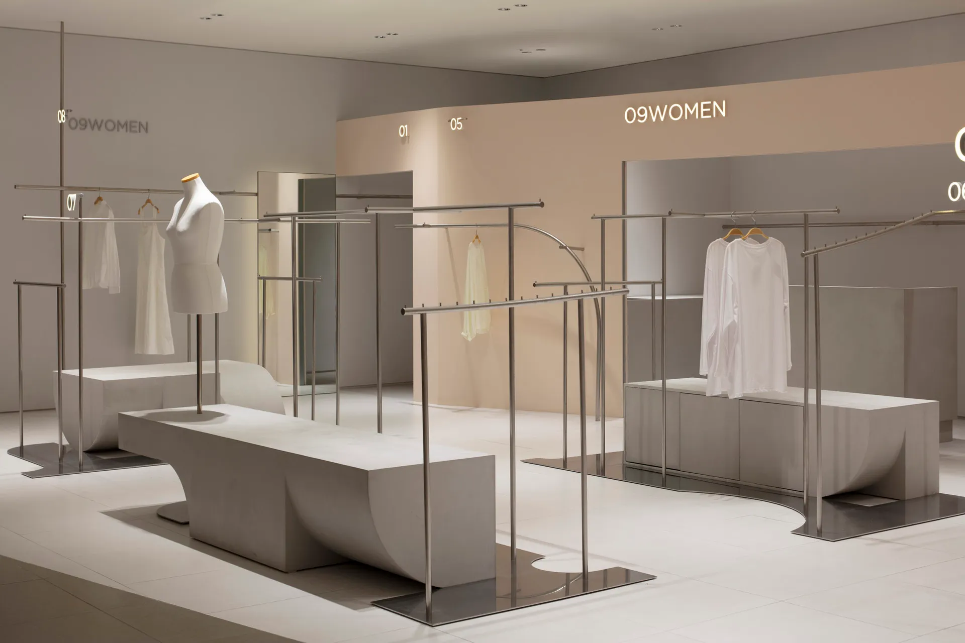 A minimalist retail shop featuring sleek steel racks and white concrete furniture.