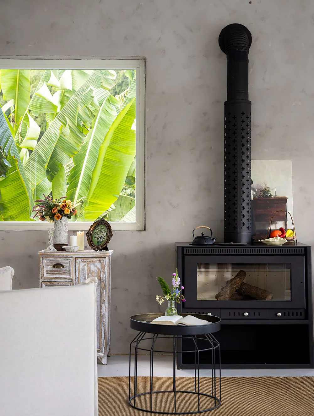 A modern living room featuring a fireplace with a black chimney, a white sofa, a small side table with a plant and a book, an