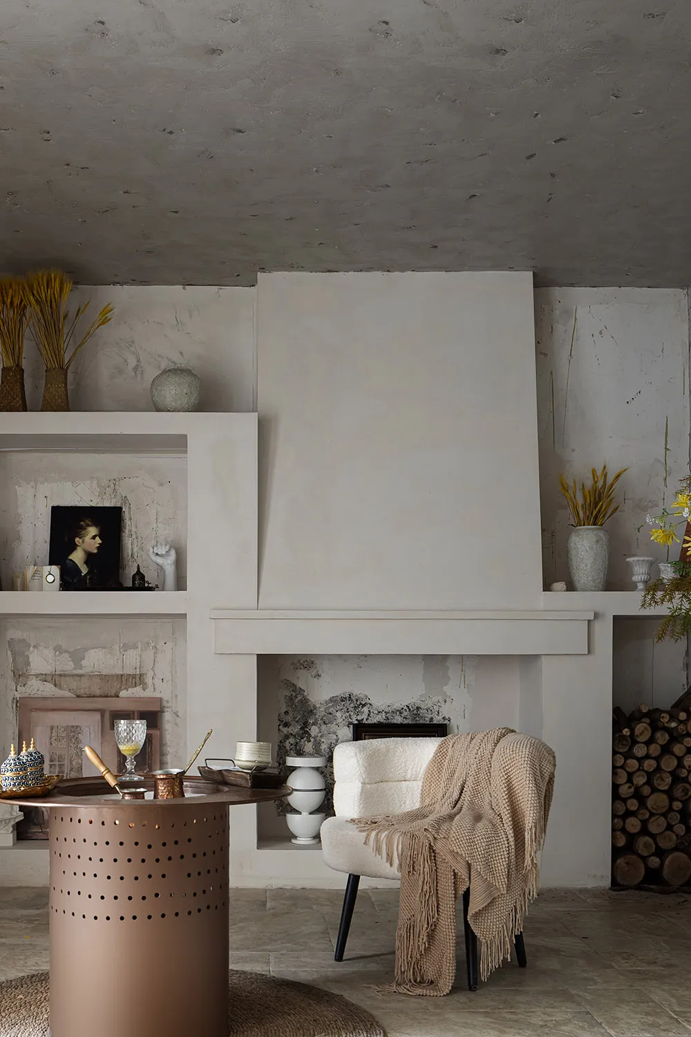 A modern minimalist living room with a concrete fireplace, wooden armchair with a beige throw blanket, and a circular metalli
