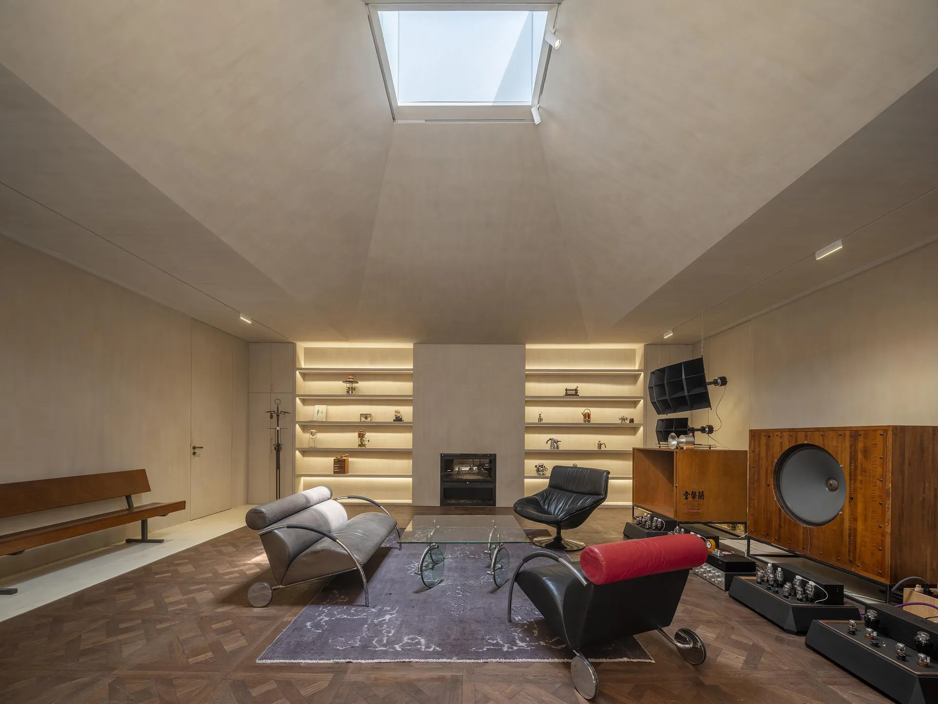 Modern industrial living room with high ceilings, skylight, wooden flooring, and minimalist furniture.