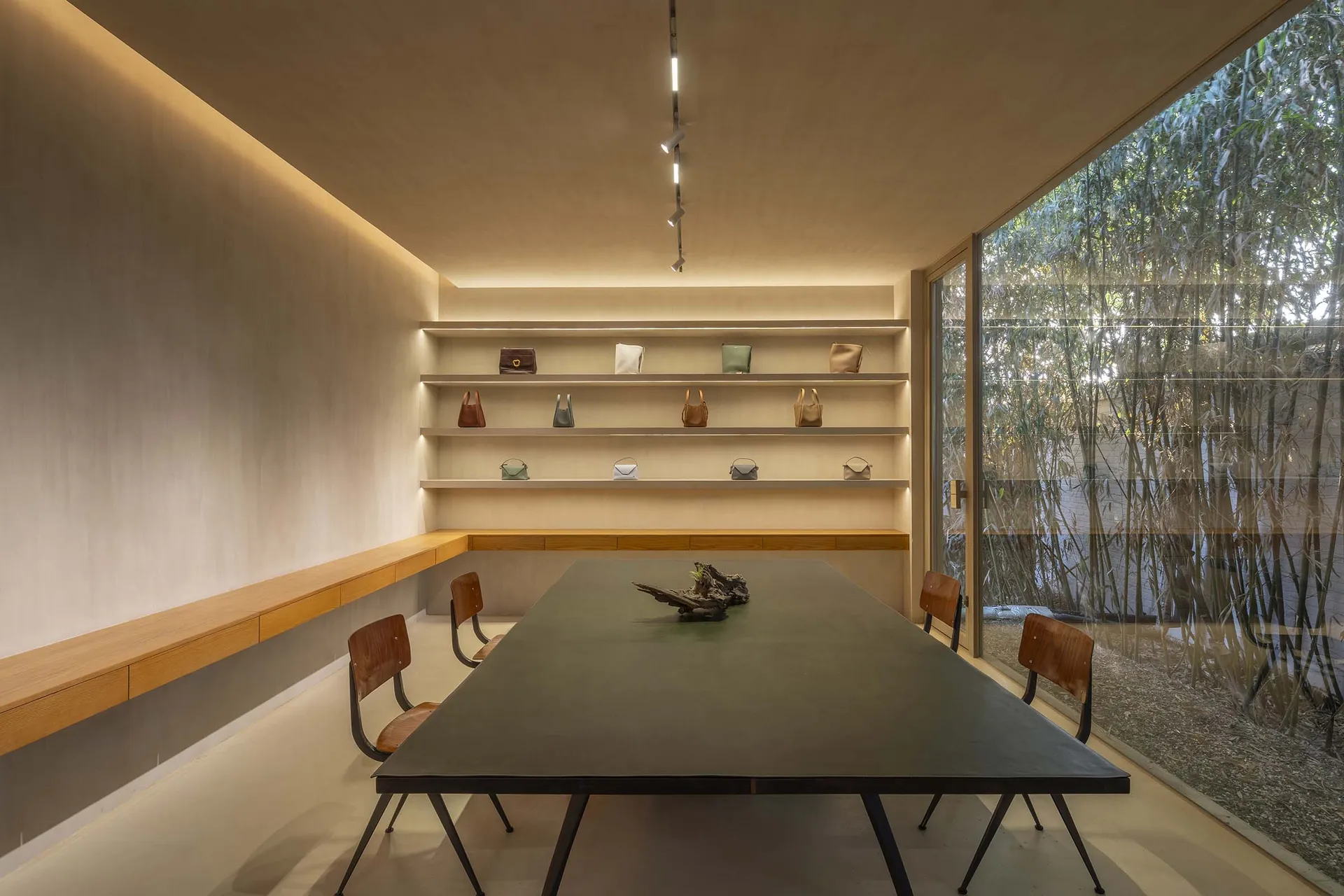 A modern conference room featuring a table, chairs, and shelves with bags, surrounded by a bamboo garden.