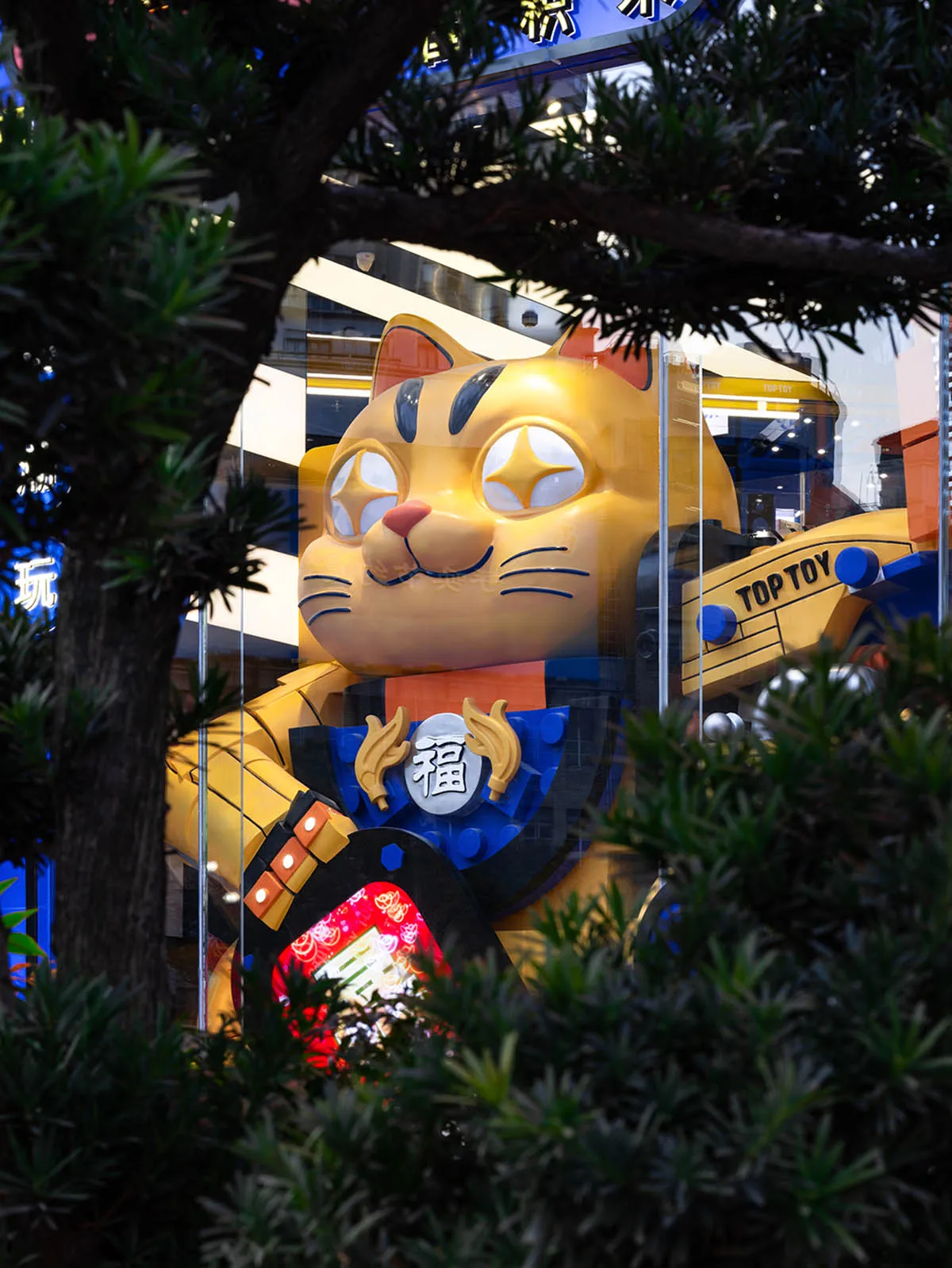 A large, colorful toy cat display in a retail storefront window.