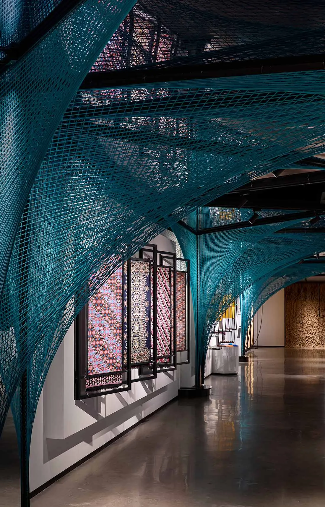 Modern architecture exhibition space with turquoise metal cable net ceiling structure.