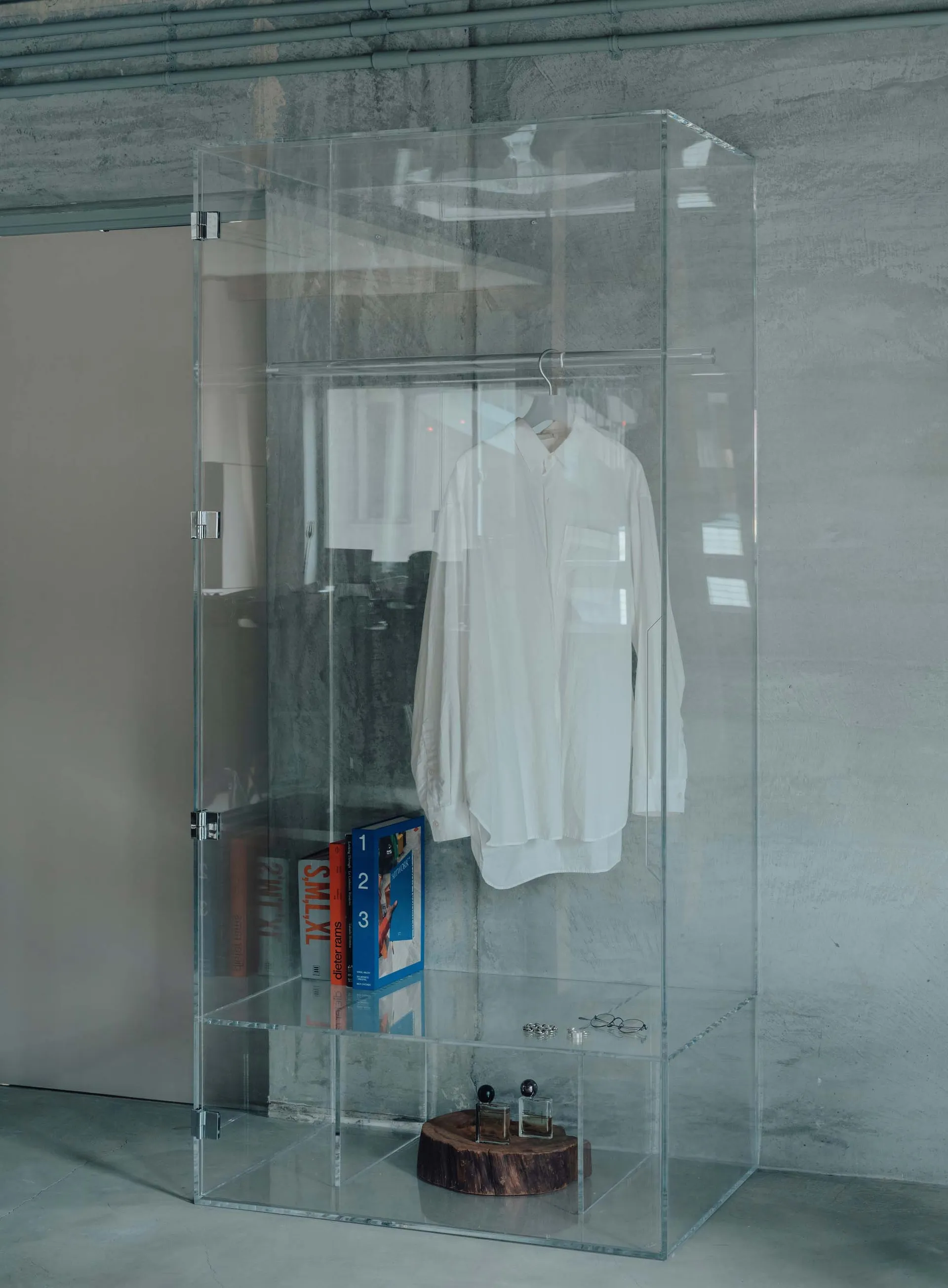 A minimalist glass display closet featuring a white shirt on a hanger.