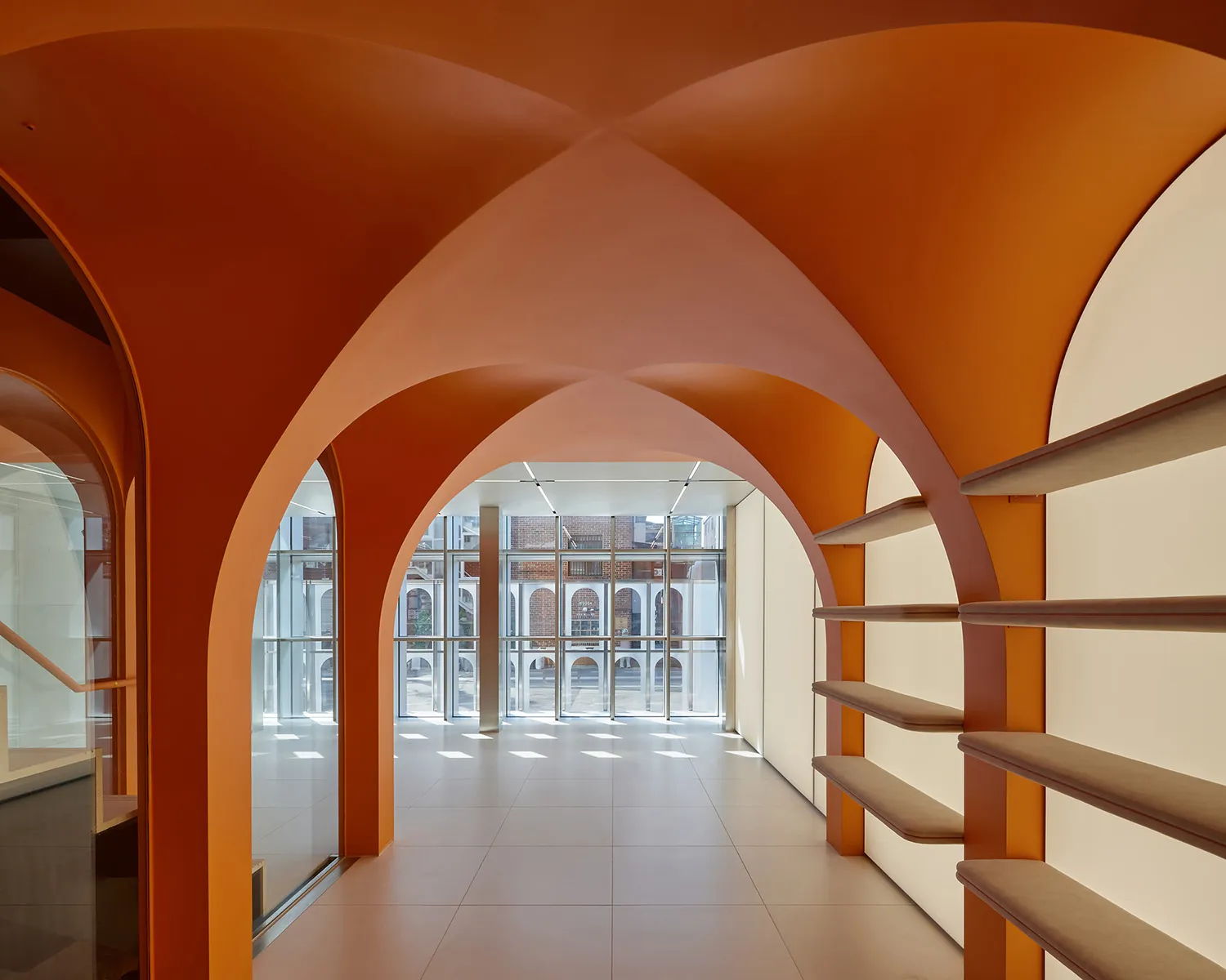 A modern lobby featuring orange concrete arches and shelving units with cushioned benches.
