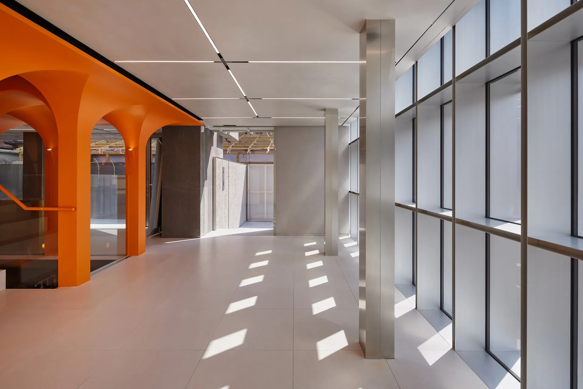 A modern office hallway with concrete walls and flooring, featuring arched doorways and windows.