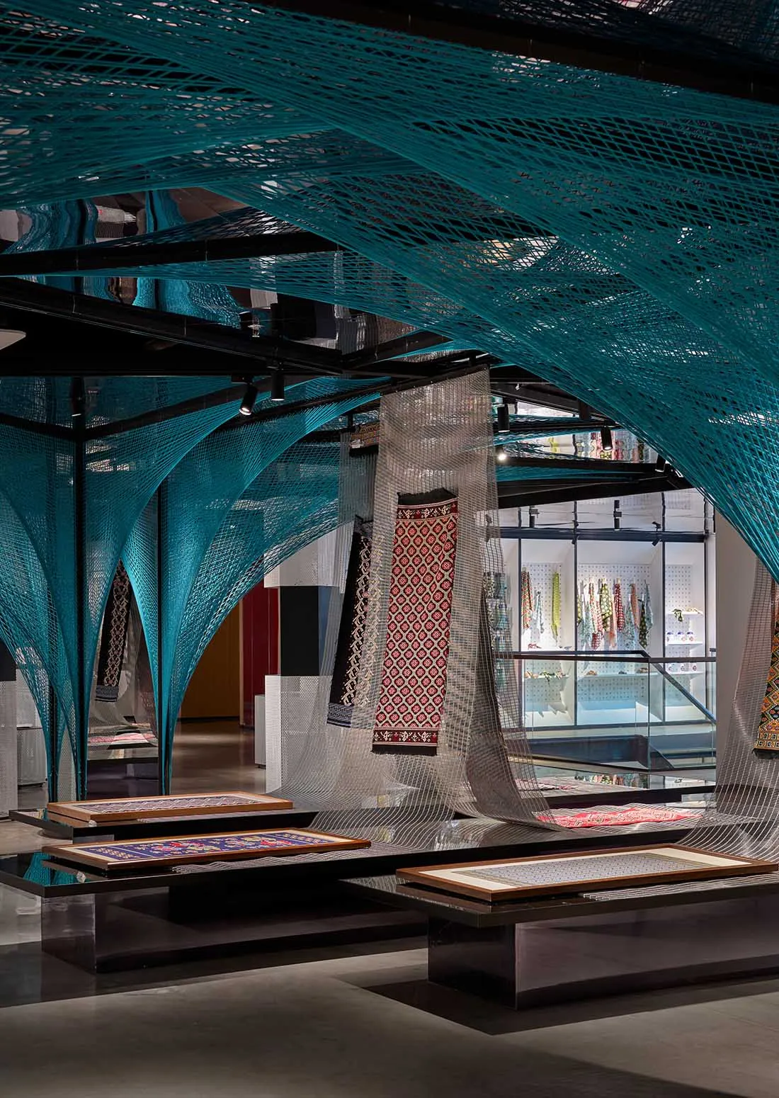 A modern retail store display featuring intricate blue netting and colorful textiles on tables and shelves.