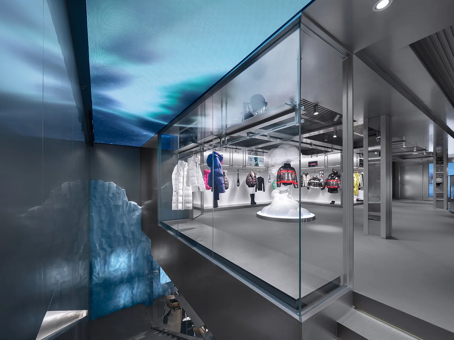 Modern retail store with glass walls displaying winter clothing on mannequins against a blue sky background.