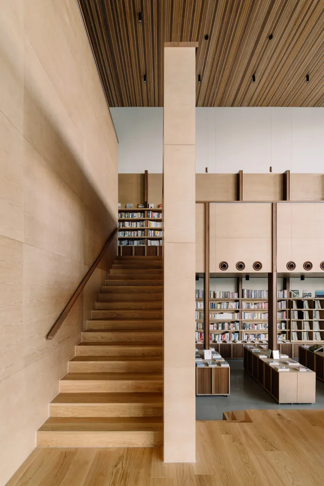A modern industrial-style library with dual-level wooden shelves and a wooden staircase.