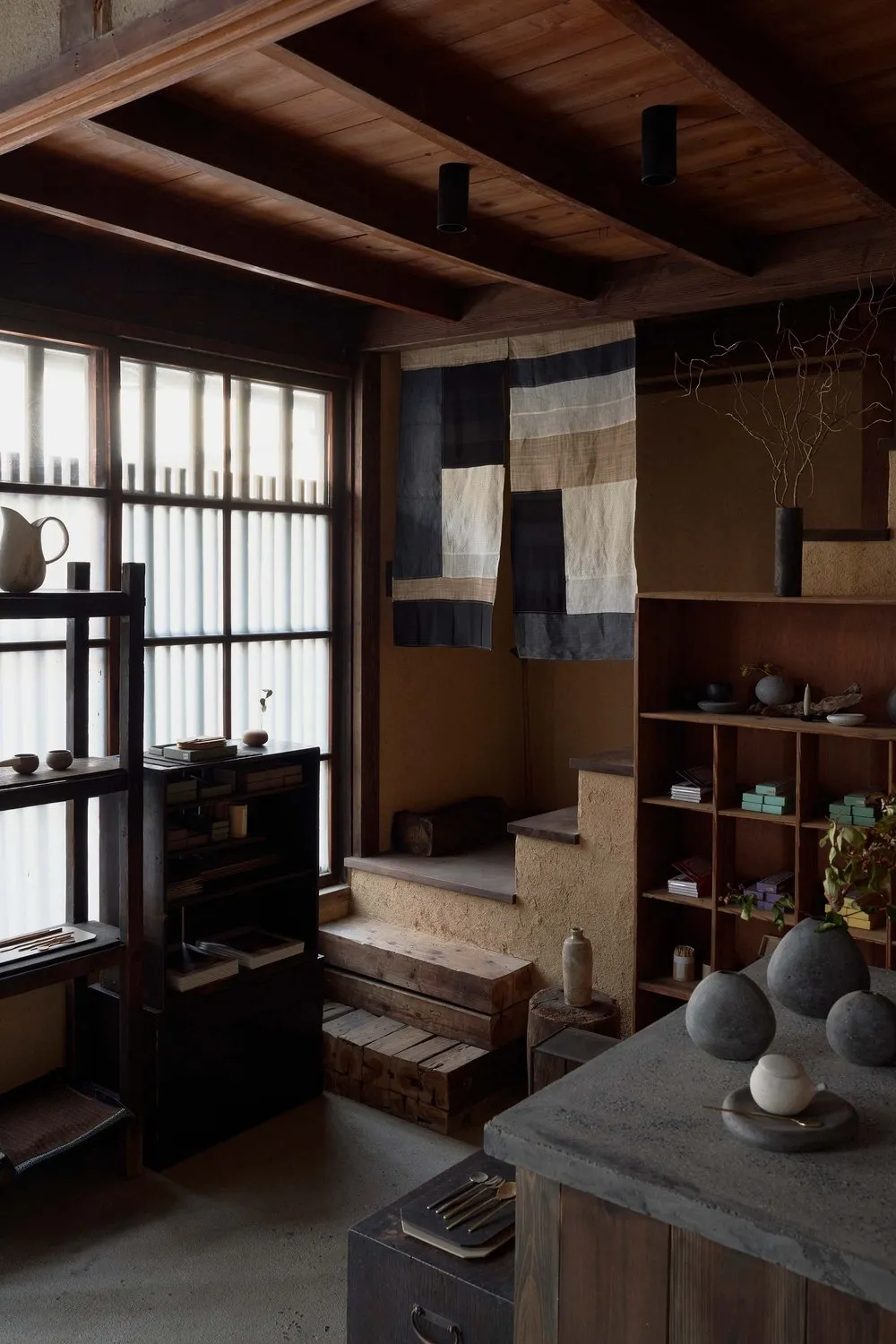 A minimalist residential kitchen featuring wooden elements, stone surfaces, and fabric accents.