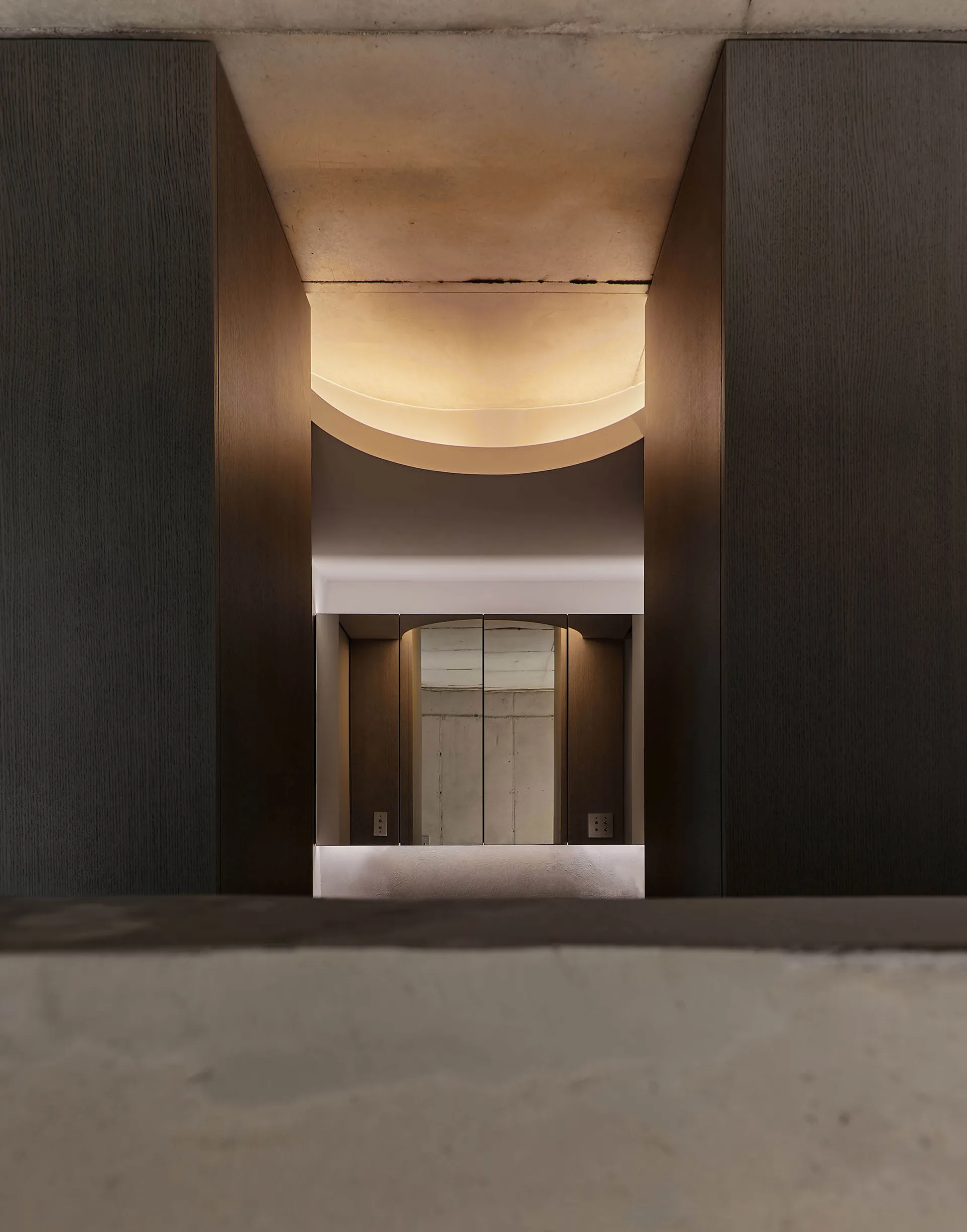 A modern entrance hall with a concrete ceiling and floor, featuring illuminated architectural details.