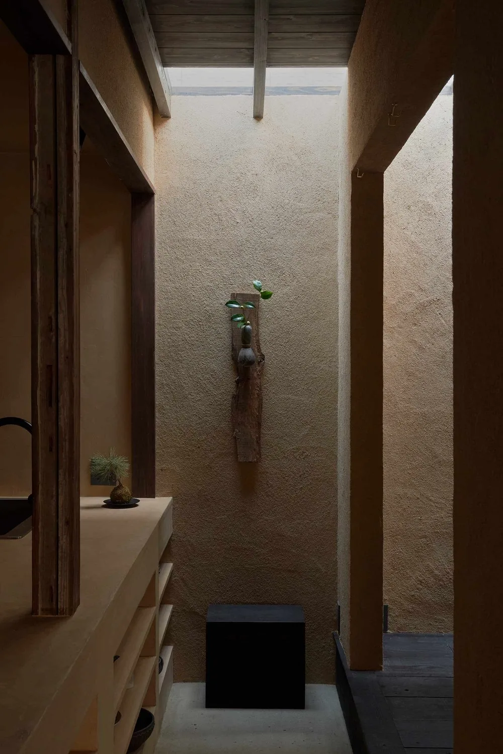 A minimalist interior design featuring concrete walls, a wooden beam, and a small vase with greenery.