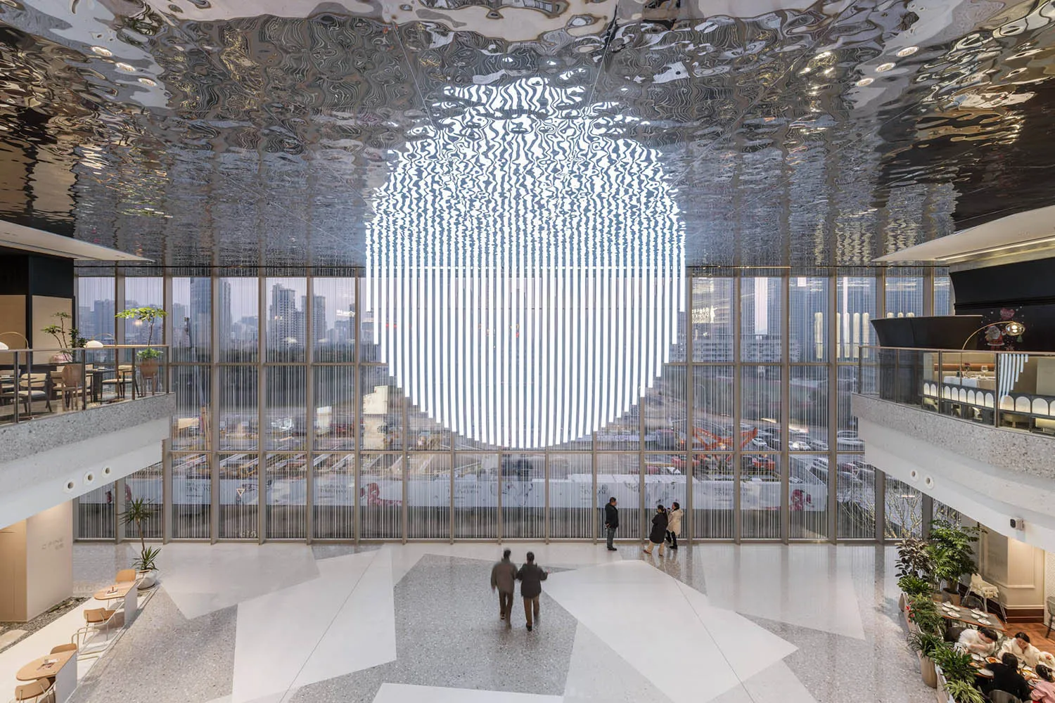 Modern lobby interior featuring metallic ceiling, glass windows, and concrete floor, with a cityscape view outside.