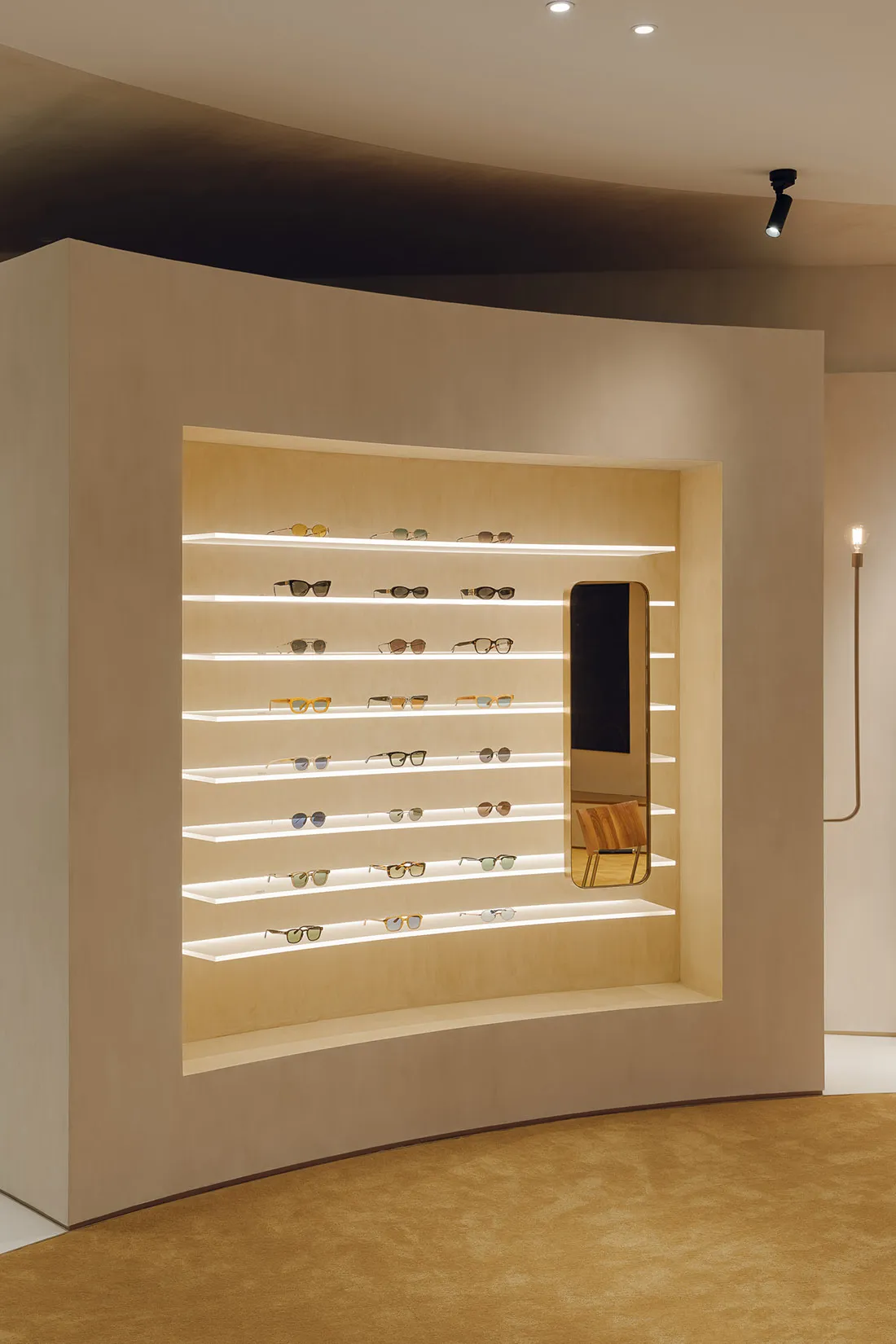 A modern retail display wall showcasing various eyeglasses on illuminated shelves.