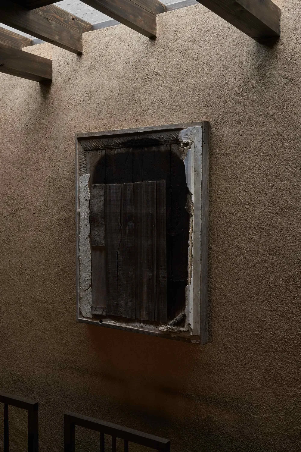 An industrial-style window with a wooden frame set in a textured wall, with visible wear and tear.
