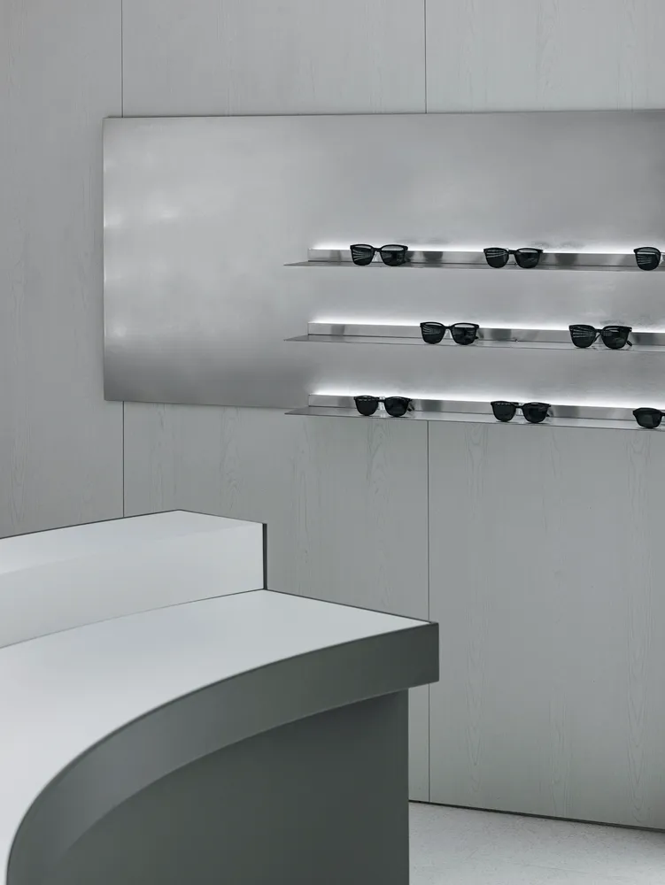 Minimalist glass counter with black metal shelves featuring black sunglasses in a retail storefront.