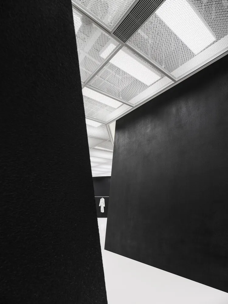 A minimalist interior space featuring black and white elements with a textured ceiling and a large, dark wall.