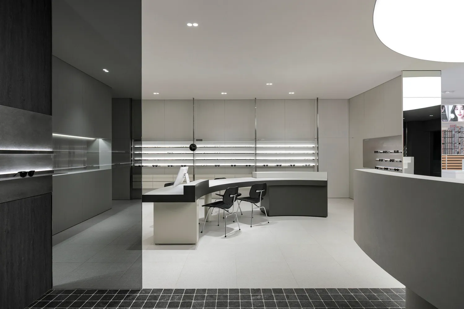 Modern retail eyewear store reception desk with minimalist design, featuring a white counter and black seating area.