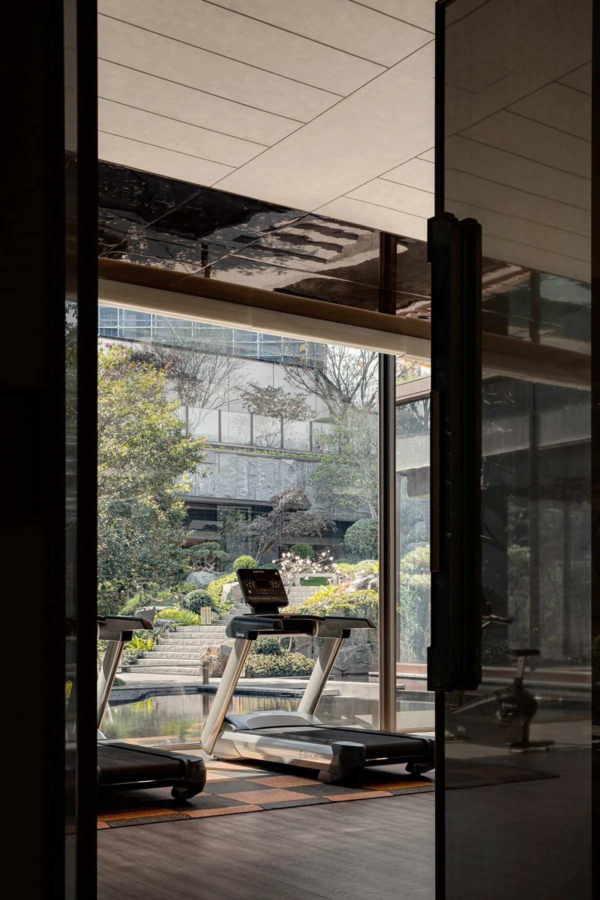 A modern fitness center with glass walls and a view of a well-maintained garden, featuring exercise equipment.