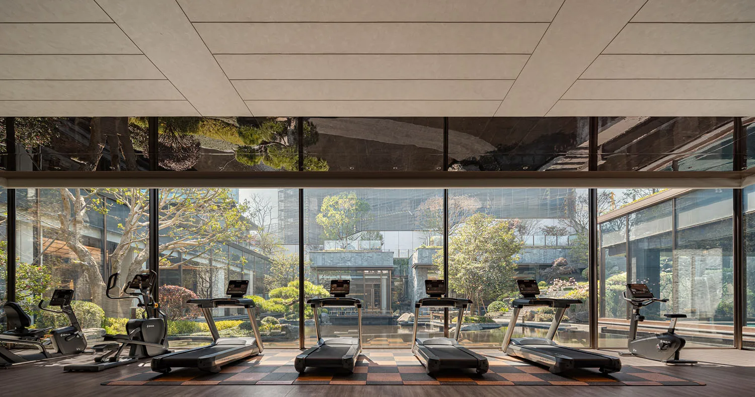 Modern gym interior with timber floor pattern and large windows overlooking greenery.