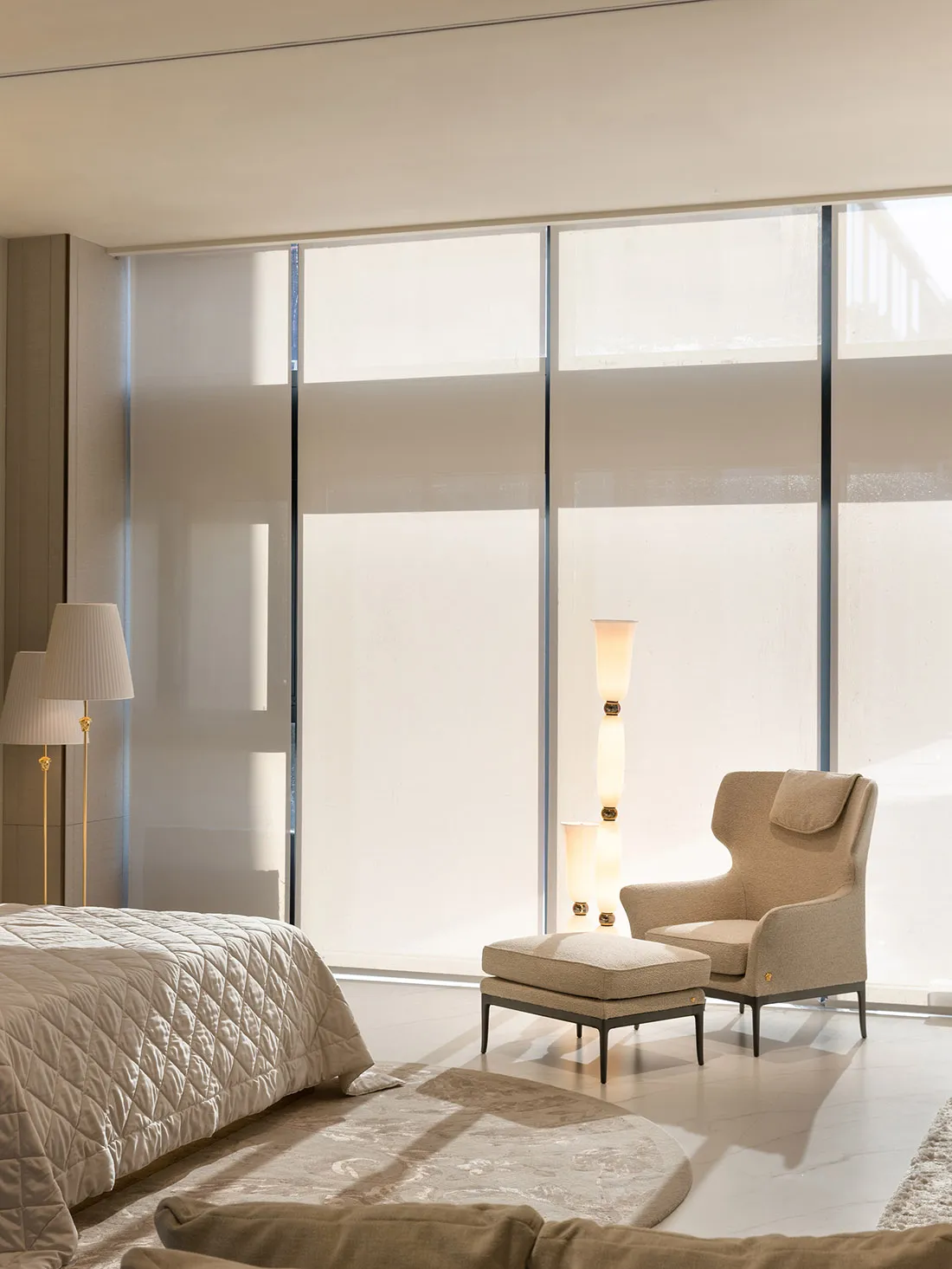 A serene bedroom with a neutral color palette, featuring a bed, armchair, and floor lamp.