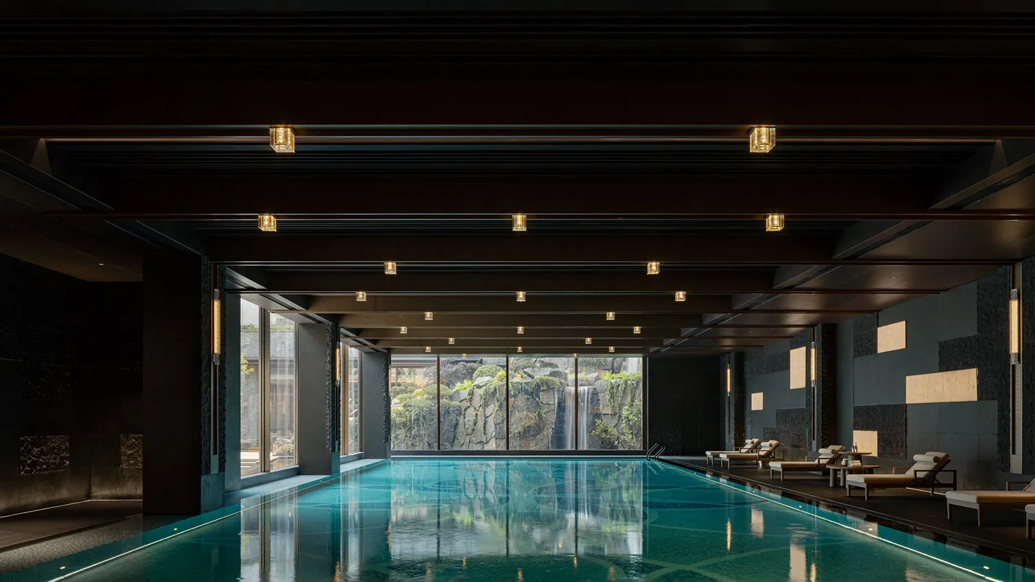 A modern swimming pool interior with concrete walls and a reflection of the ceiling lights on the water surface.