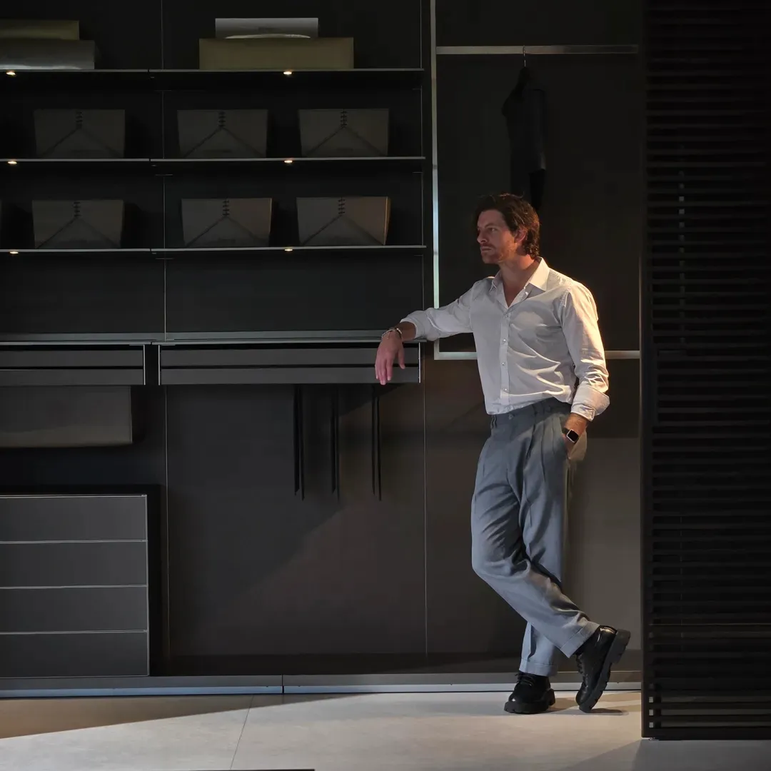 A man in a white shirt is leaning against metal shelves in a modern closet.
