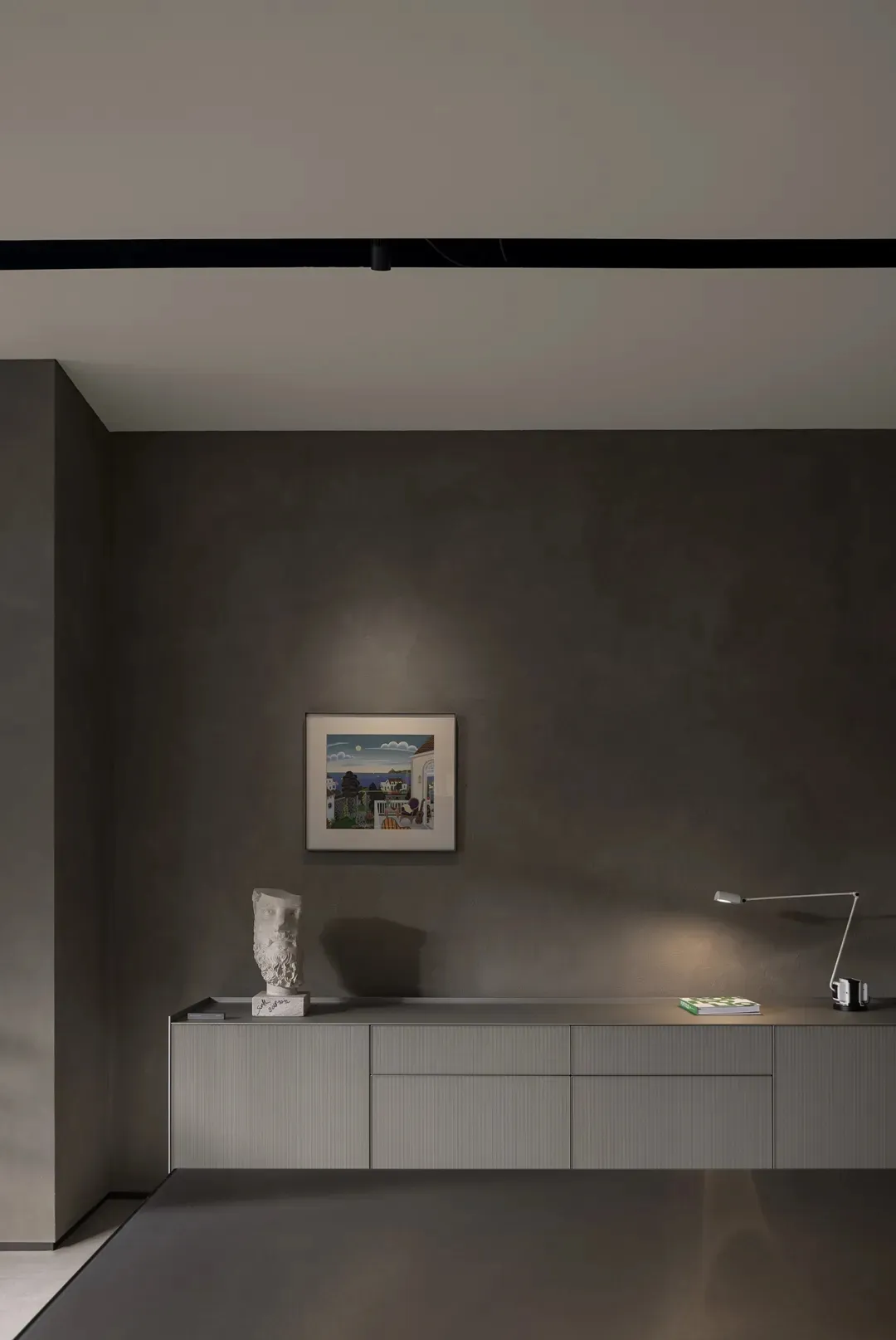 A minimalist alcove with concrete walls, featuring a framed painting and a bust sculpture on a sideboard.