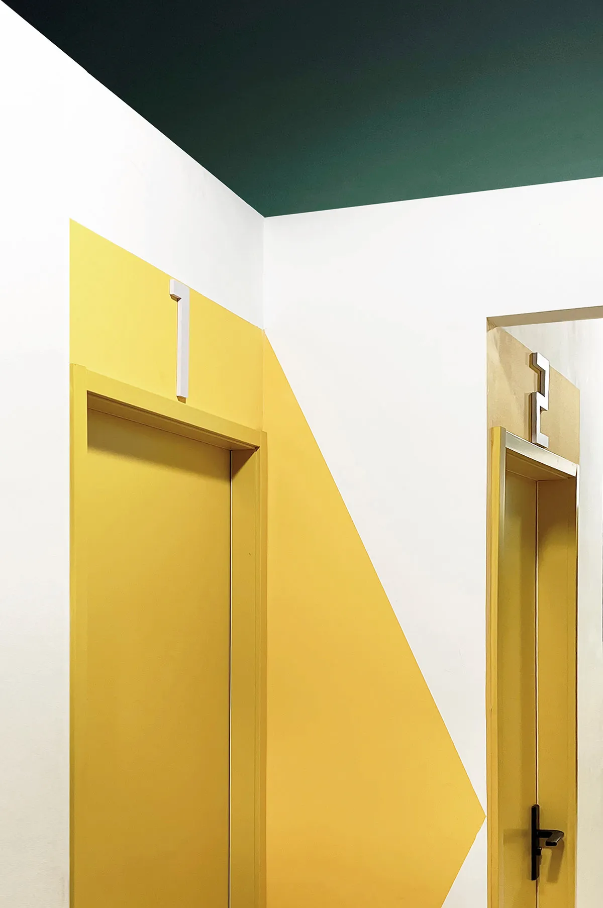 A close-up of a yellow door with a color-blocked pattern on a white wall.