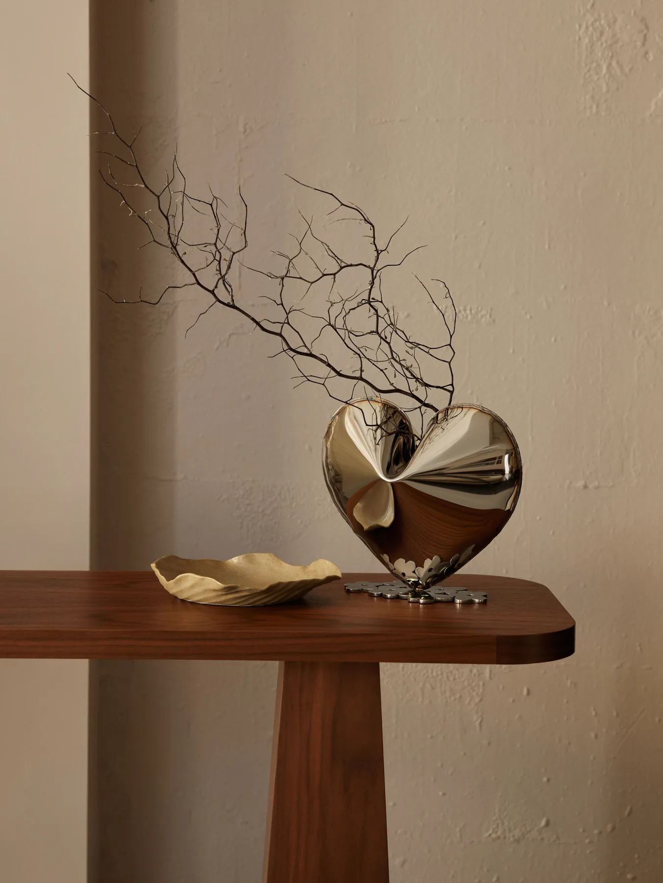 A heart-shaped metal vase with twigs inside on a wooden table.