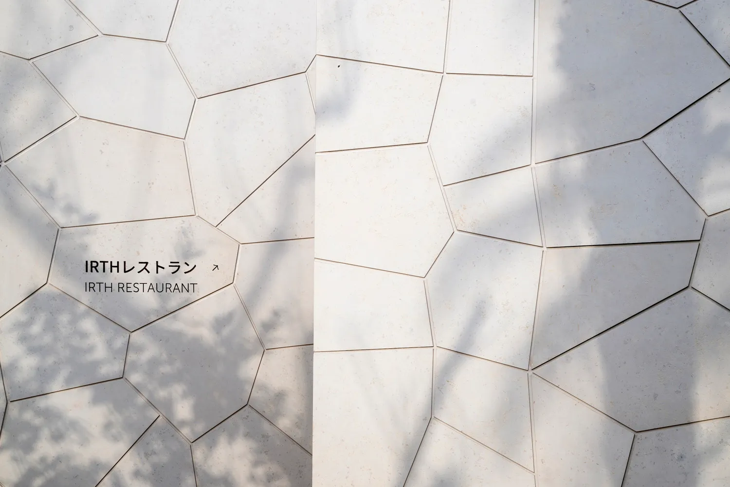 Modern exterior made of concrete tiles with irregular shapes and shadows from trees.