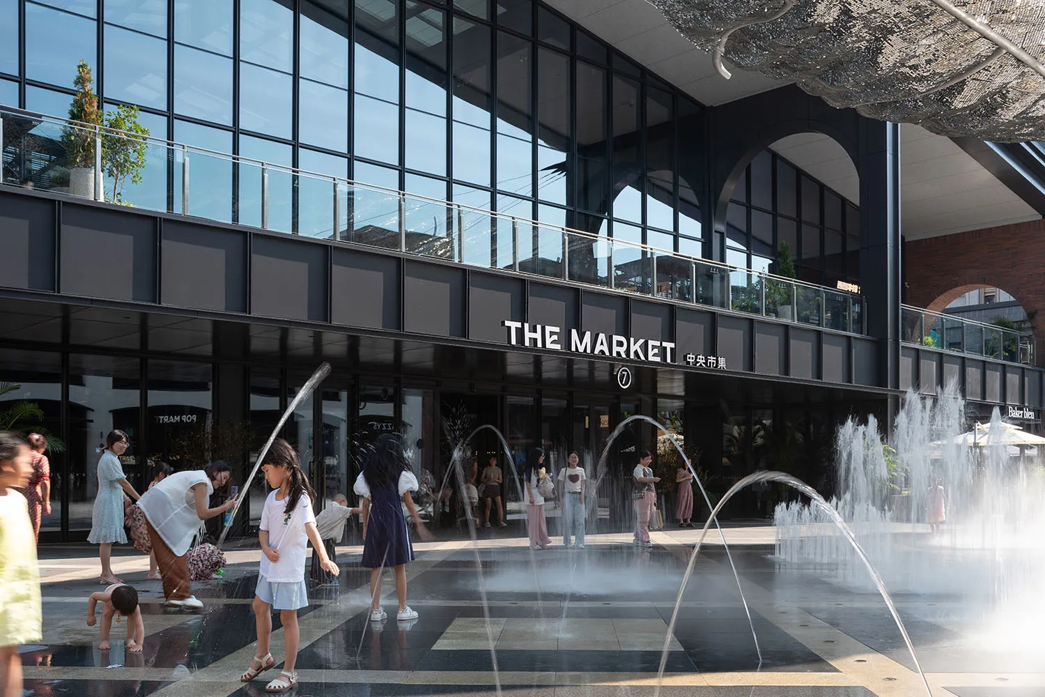 People enjoying a sunny day at a modern outdoor plaza with a glass fountain.