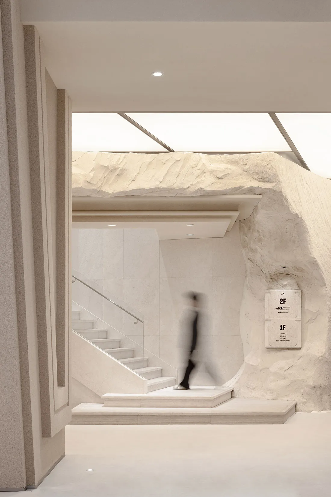 A minimalist interior space featuring a concrete staircase with a glass railing, illuminated by natural light from large wind