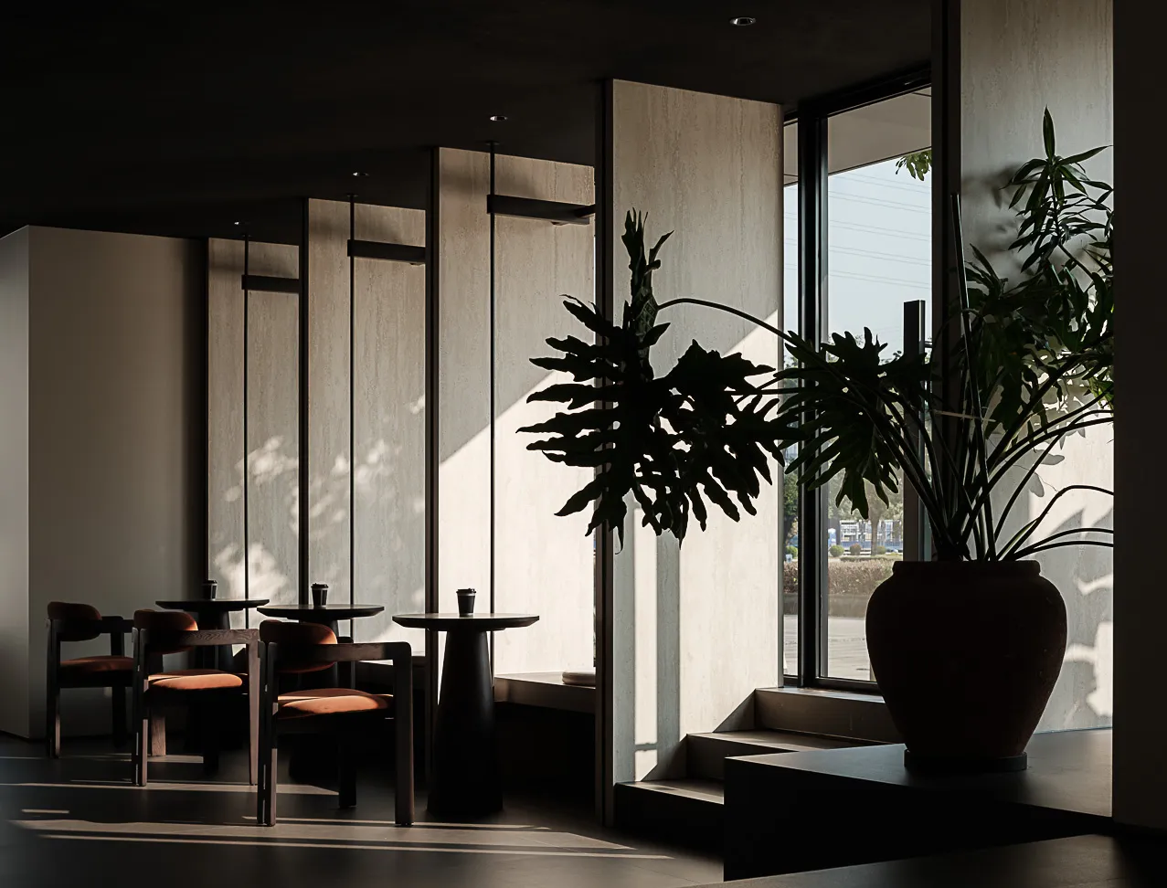 Minimalist cafe interior with concrete walls, wooden tables, and potted plants.