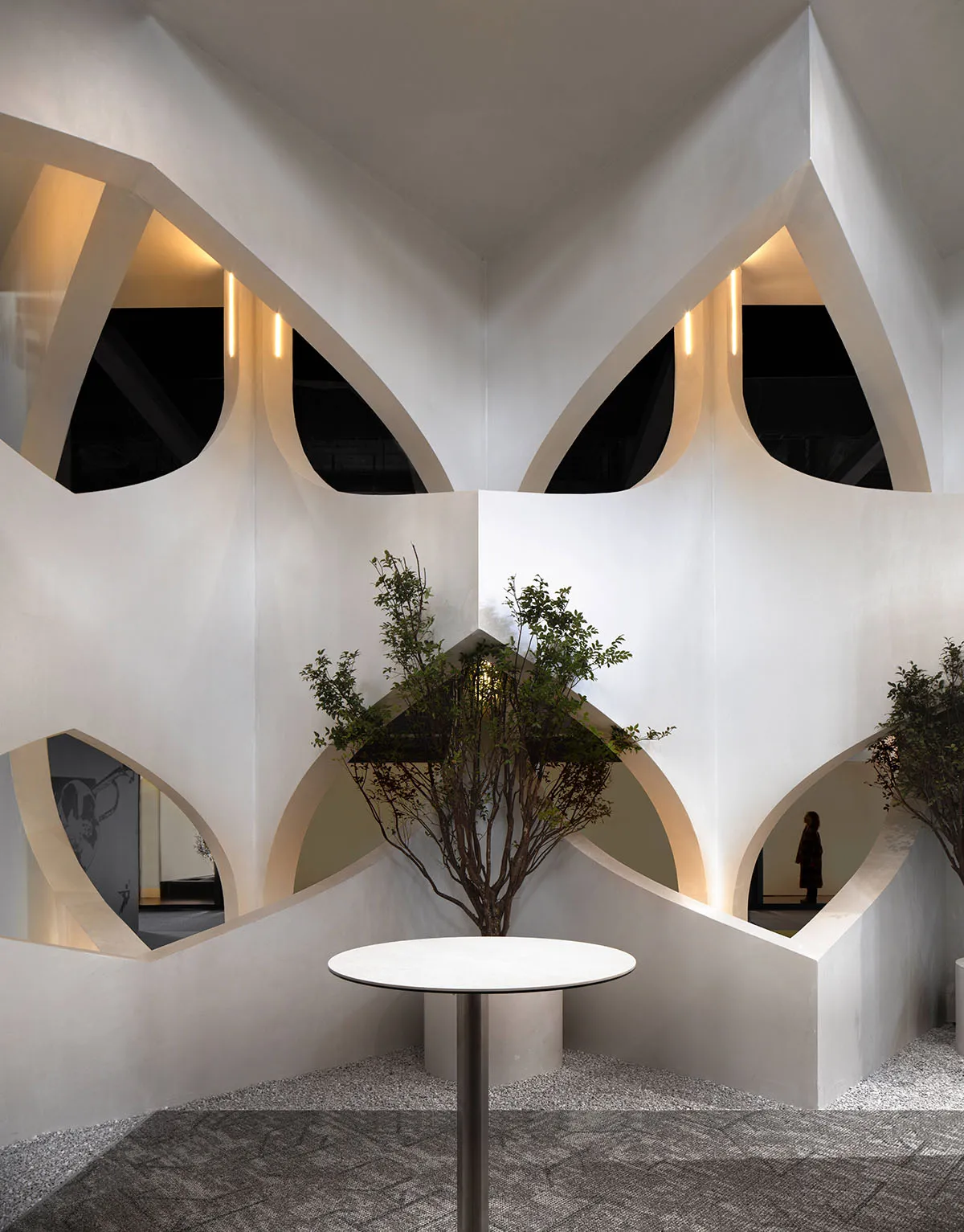 A modern interior design space featuring geometric concrete architecture, intricate lighting fixtures, and a potted green pla