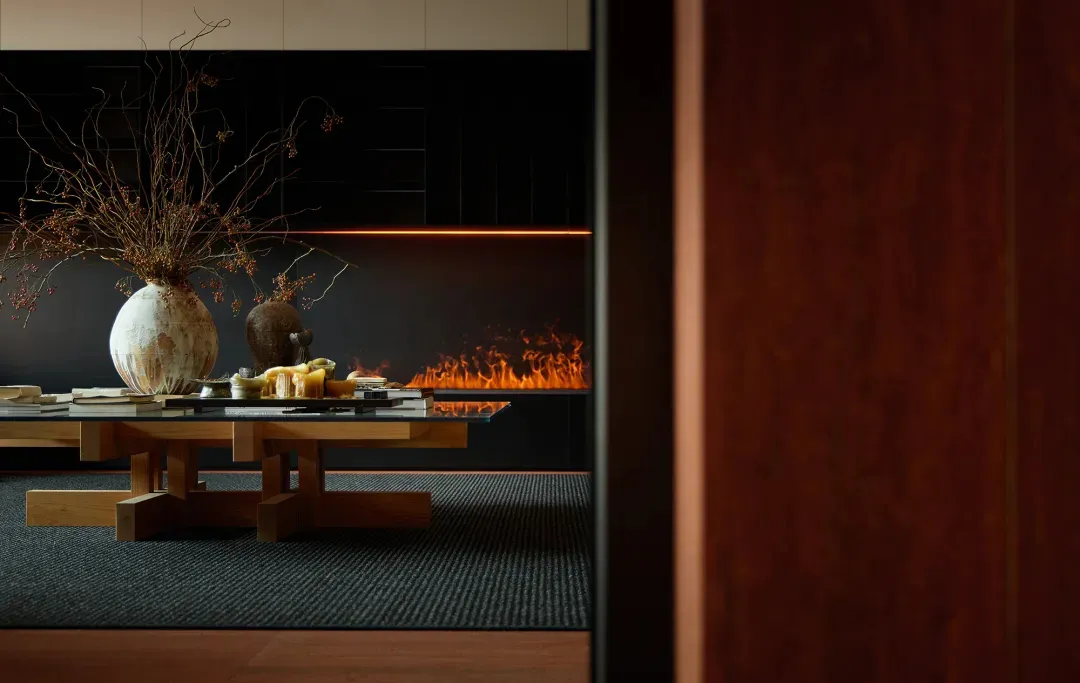 Modern living room featuring a wooden vase, a fireplace with flames, and a black rug.