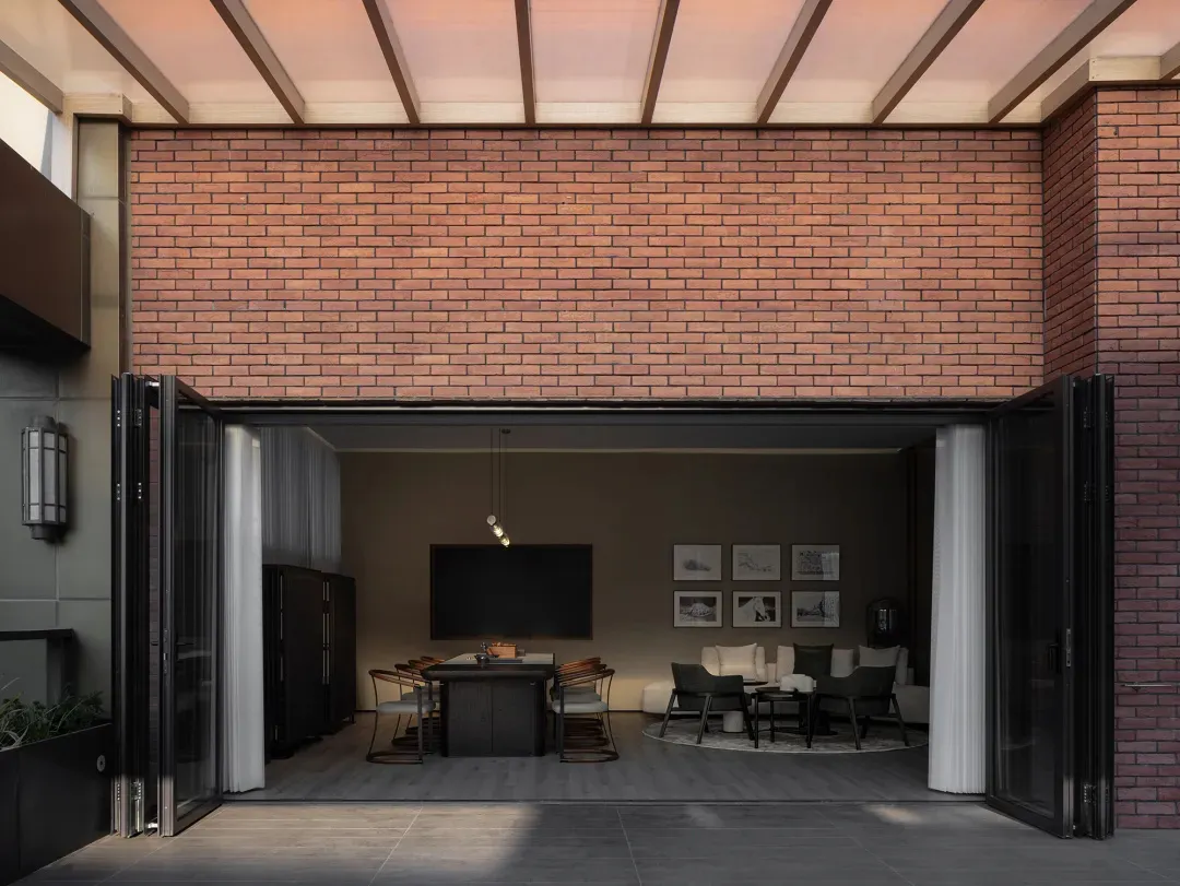 A modern living room with brick walls, featuring dark furniture and a large window.