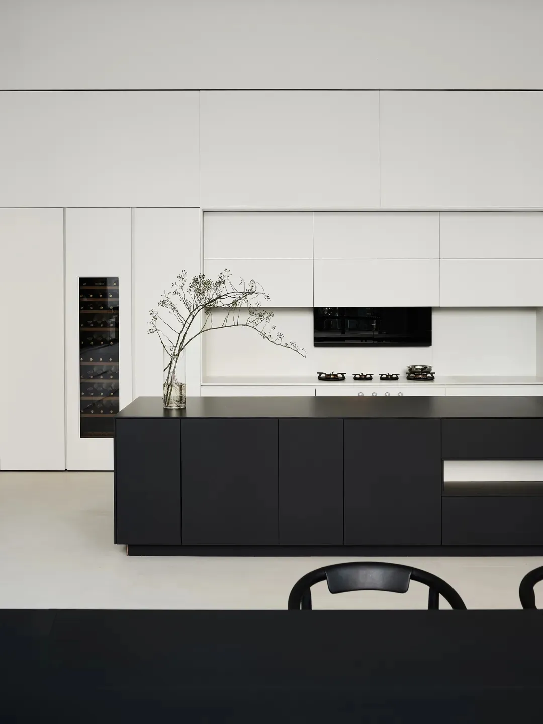 Modern, minimalist kitchen with black cabinets, white countertops, and a black island in the center of the room.