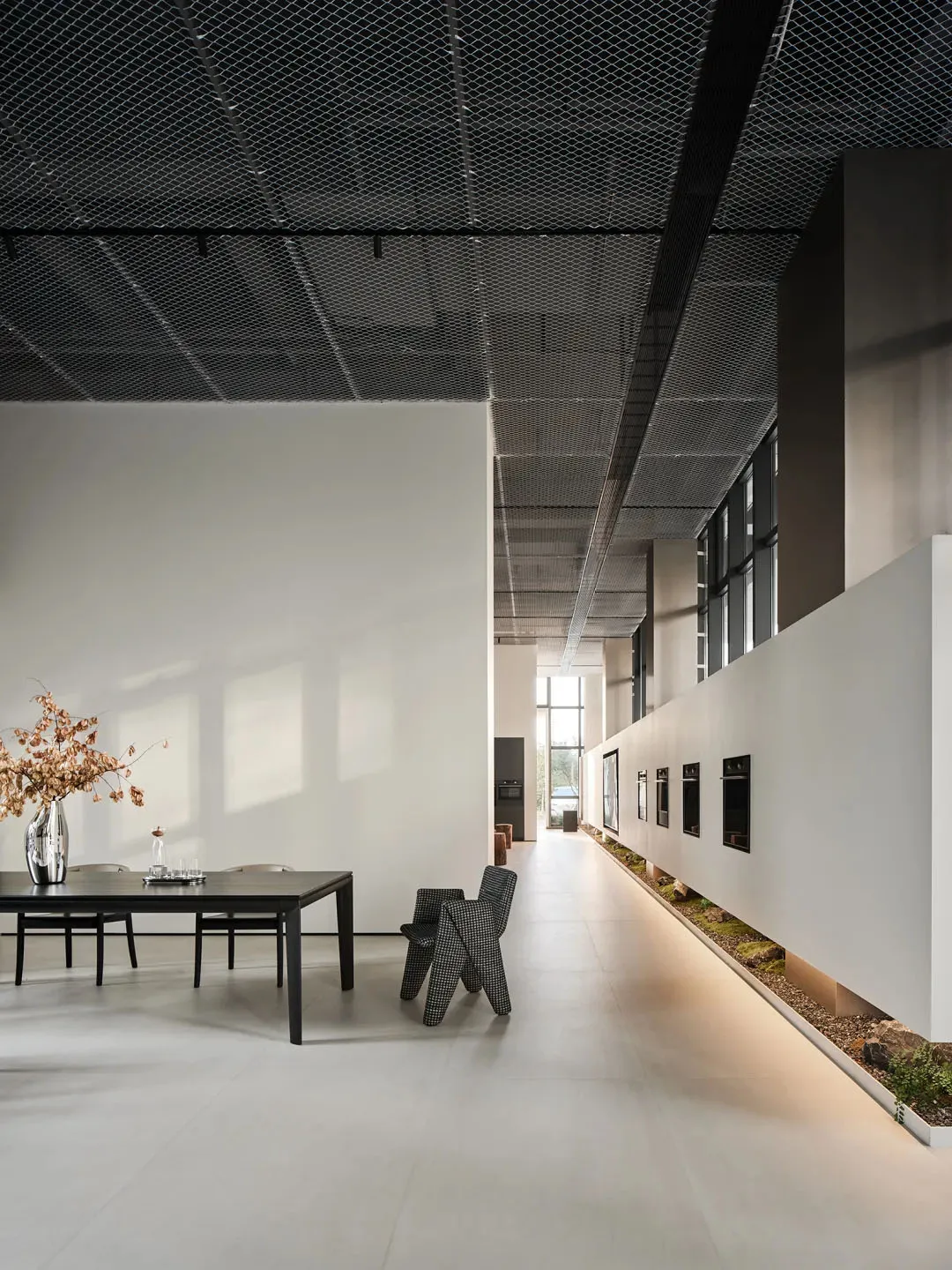 A modern commercial space with concrete and glass materials, featuring a long table with chairs and a decorative vase.