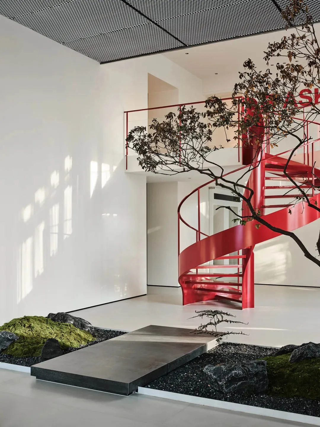 A modern office interior featuring a spiral staircase with red metal railings and a minimalist design.