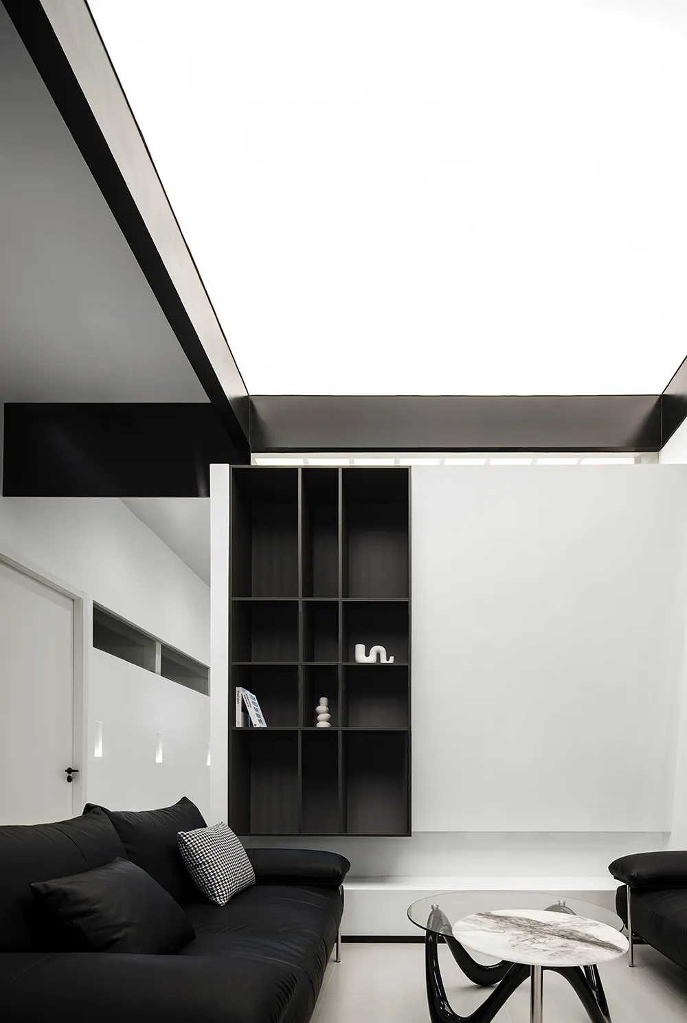 Modern minimalist living room with black leather sofas, glass coffee table, and metal shelving unit.