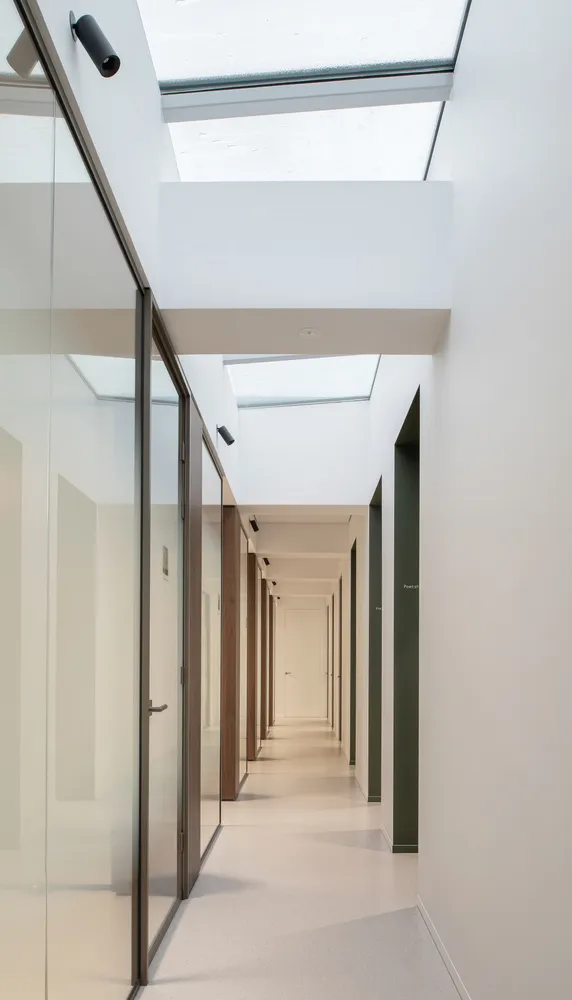 Modern office corridor featuring glass walls, wooden doors, and concrete flooring.
