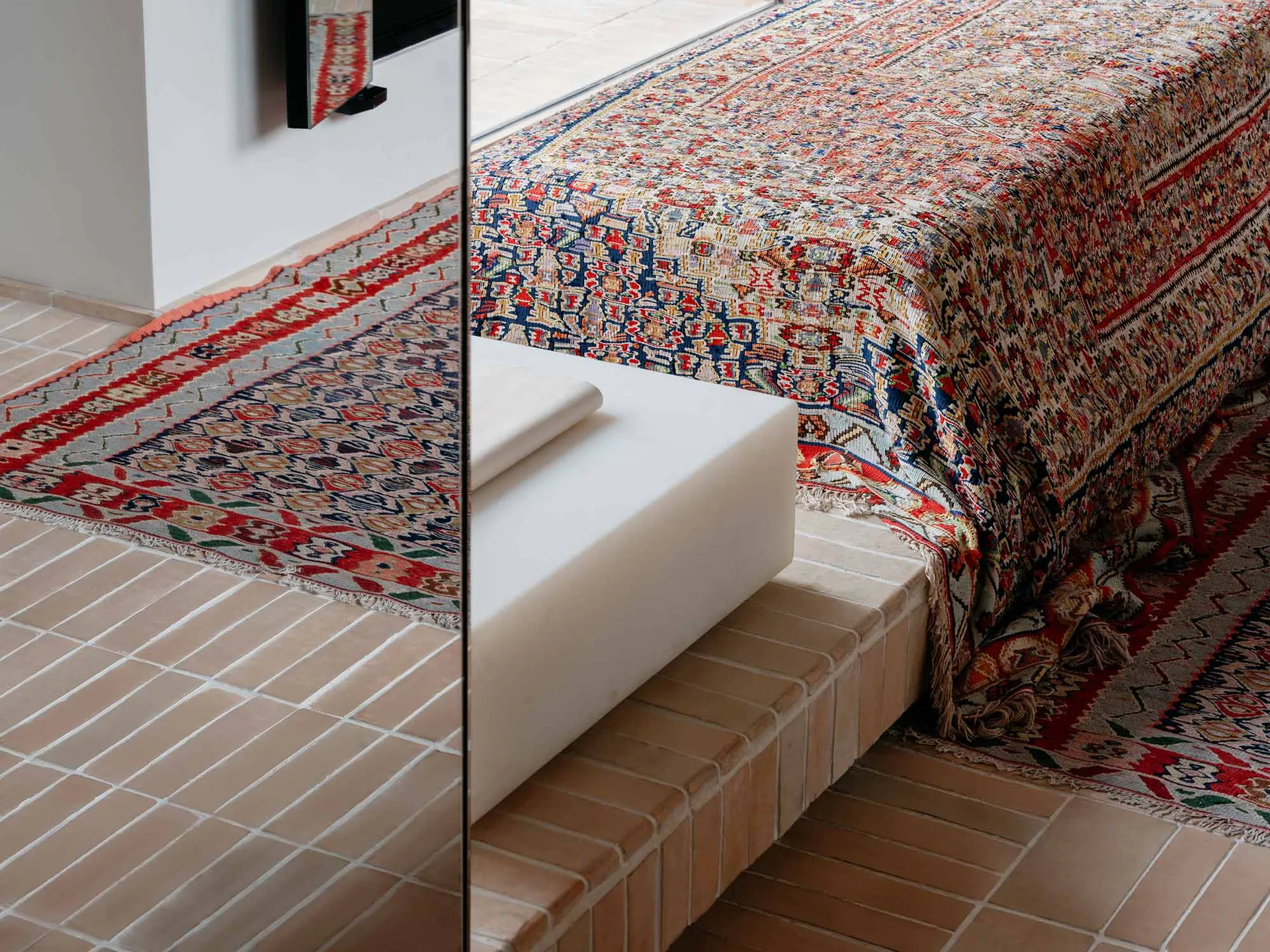 A bedroom scene featuring a wooden platform decorated with an oriental-patterned tile rug.