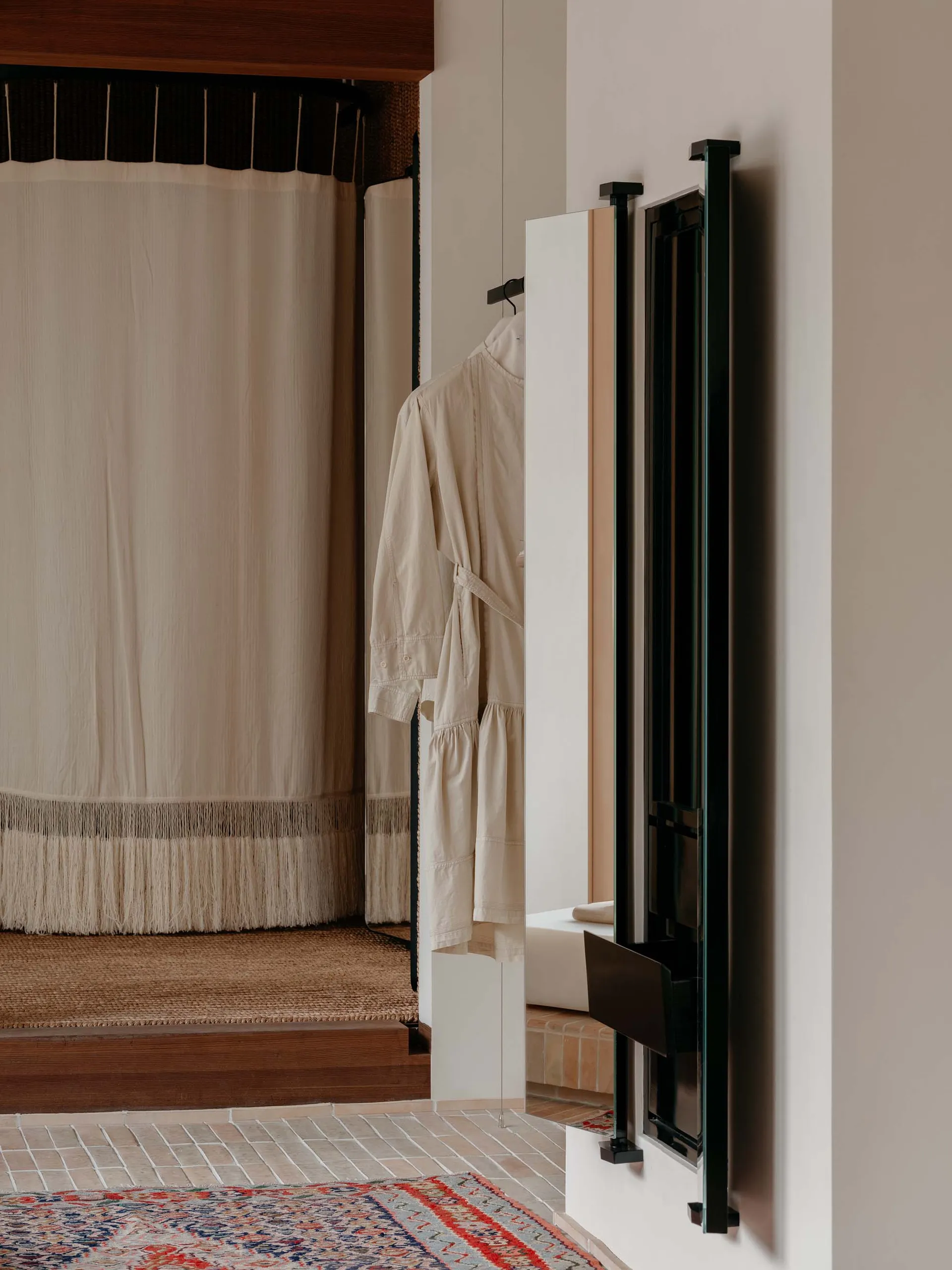 Closet entryway with a cotton curtain, a beige jacket hanging on a black coat hanger, and a tiled floor with a patterned rug.