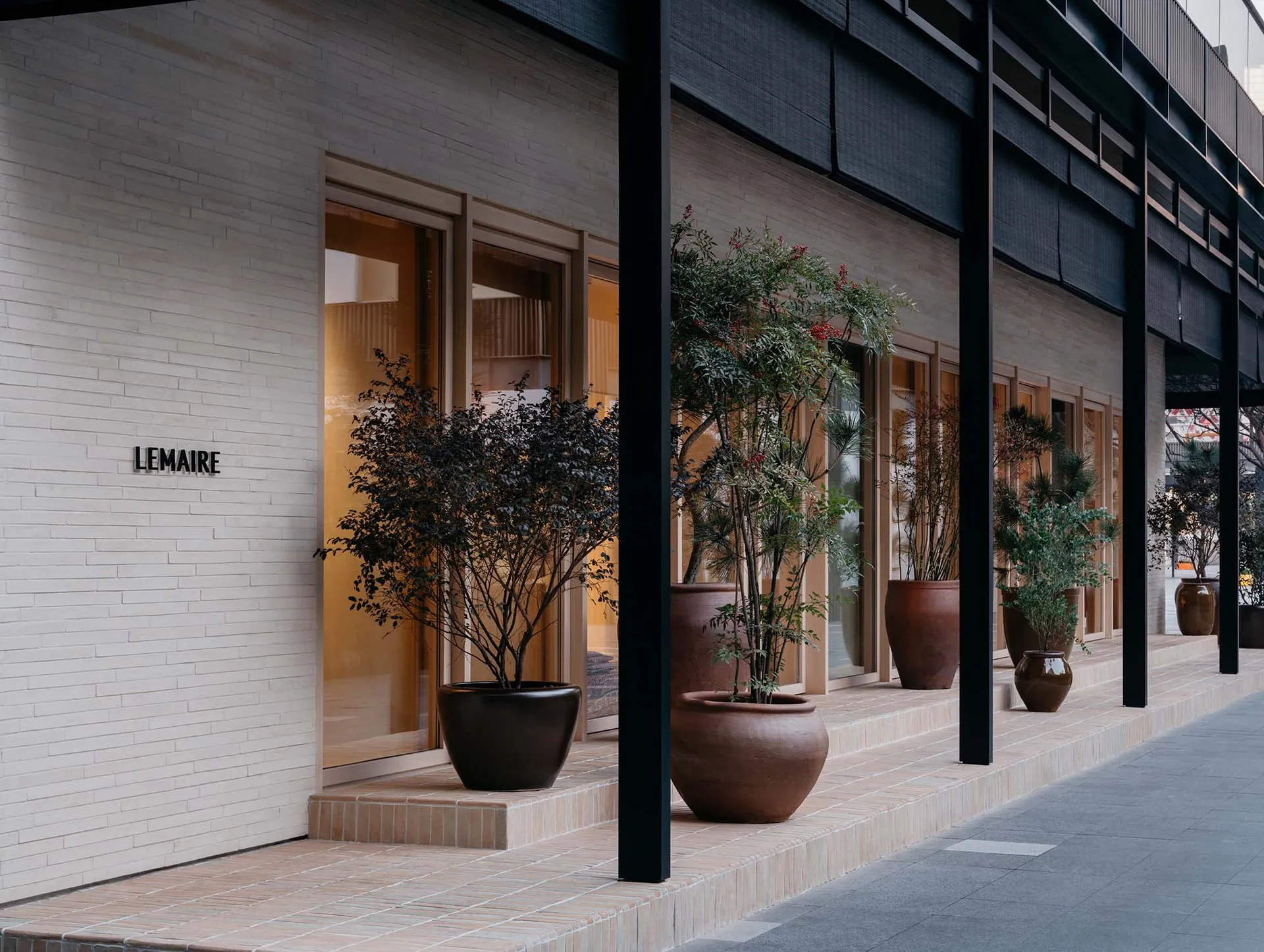 Modern retail storefront with large glass windows and potted plants in terracotta pots.