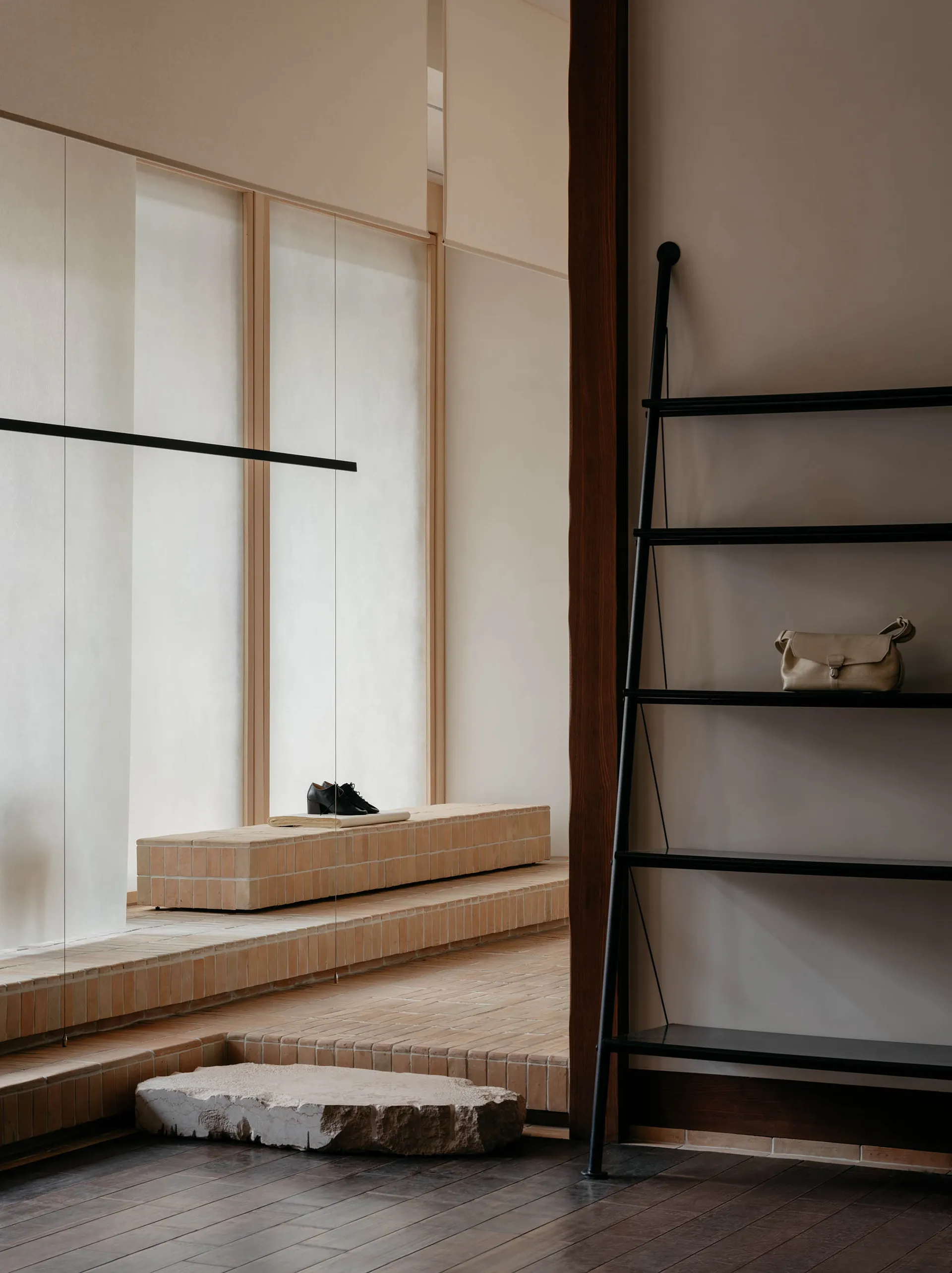 A minimalist shoe store interior with a brick counter and a black ladder with a leather bag.