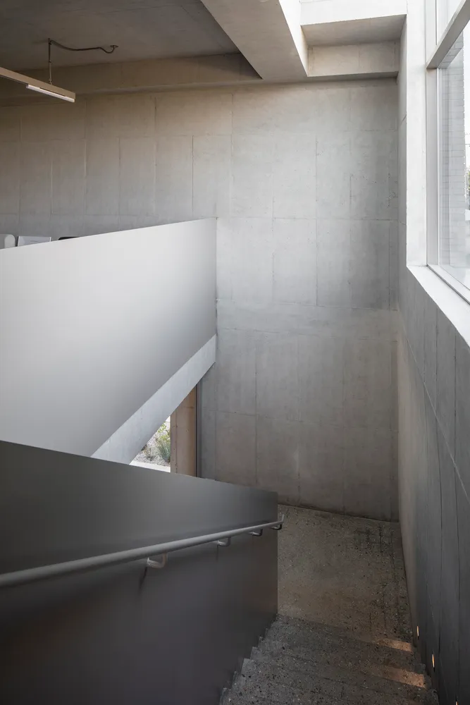 A minimalist concrete stairwell with a white railing and a window on the right side.