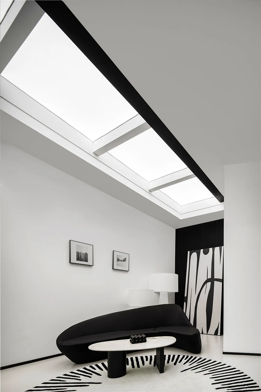 A minimalist living room with black and white decor and light streaming in from skylights.